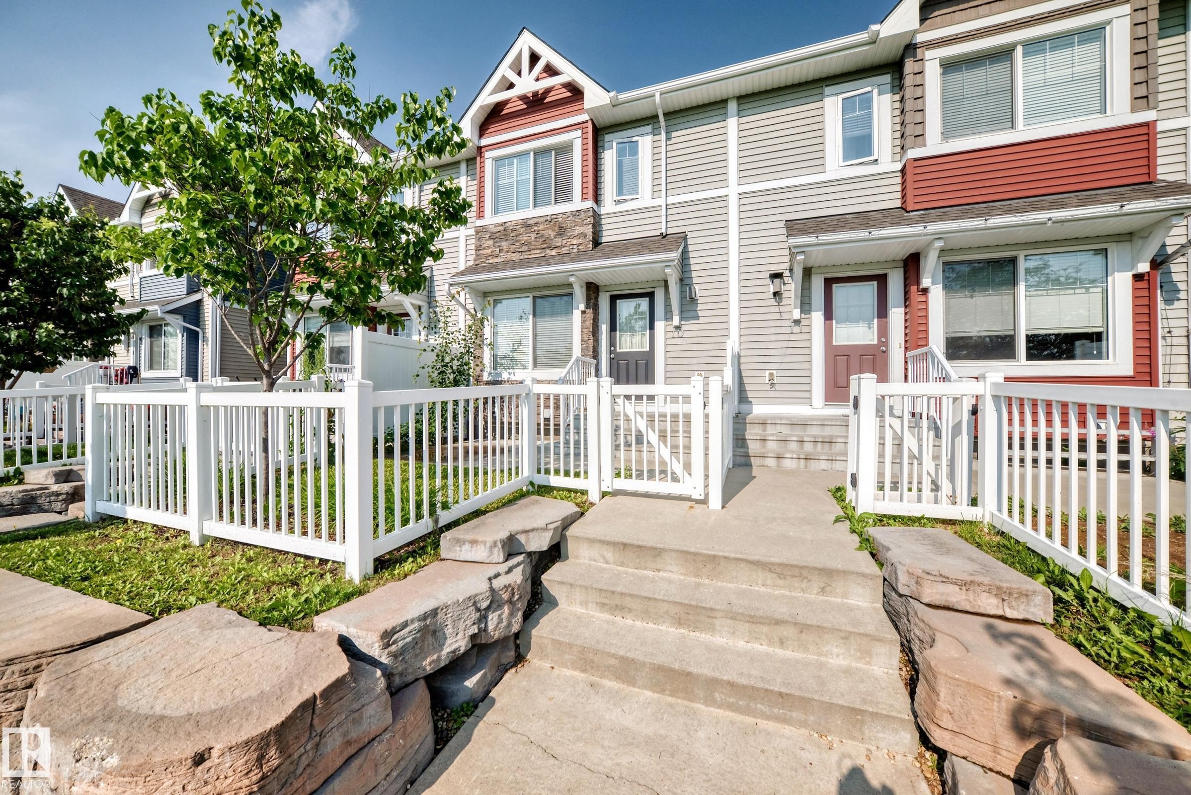 Townhome exterior featuring horizontal siding, a stone accent facade, and a white picket fence - 415 Clareview Rd Nw Nw, Edmonton, AB - Outdoor With Deck Patio Veranda With Facade