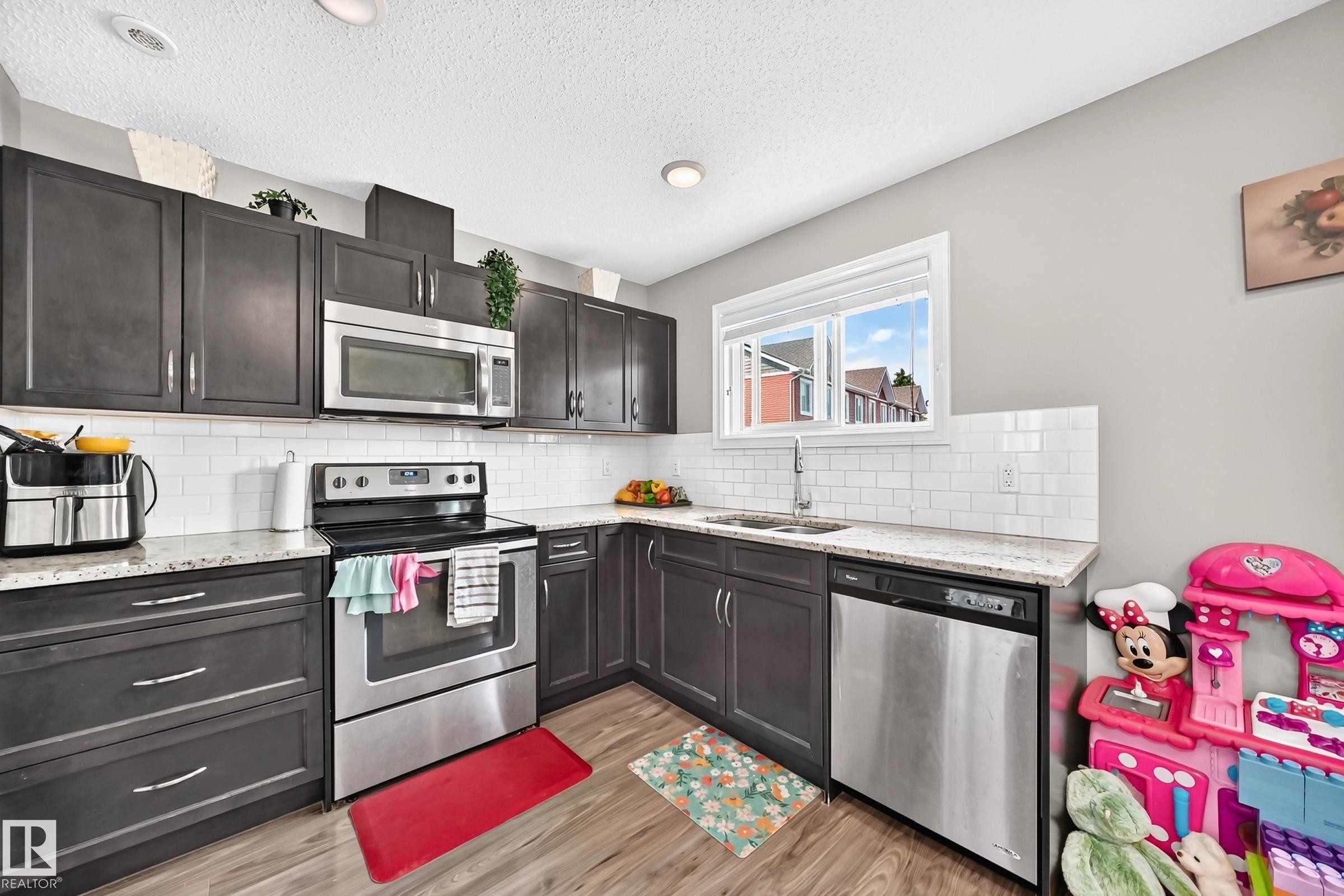 Kitchen featuring wood-finish flooring, dark cabinetry, white subway tile backsplash, and granite-style countertops - 415 Clareview Rd Nw Nw, Edmonton, AB - Indoor Photo Showing Kitchen With Upgraded Kitchen