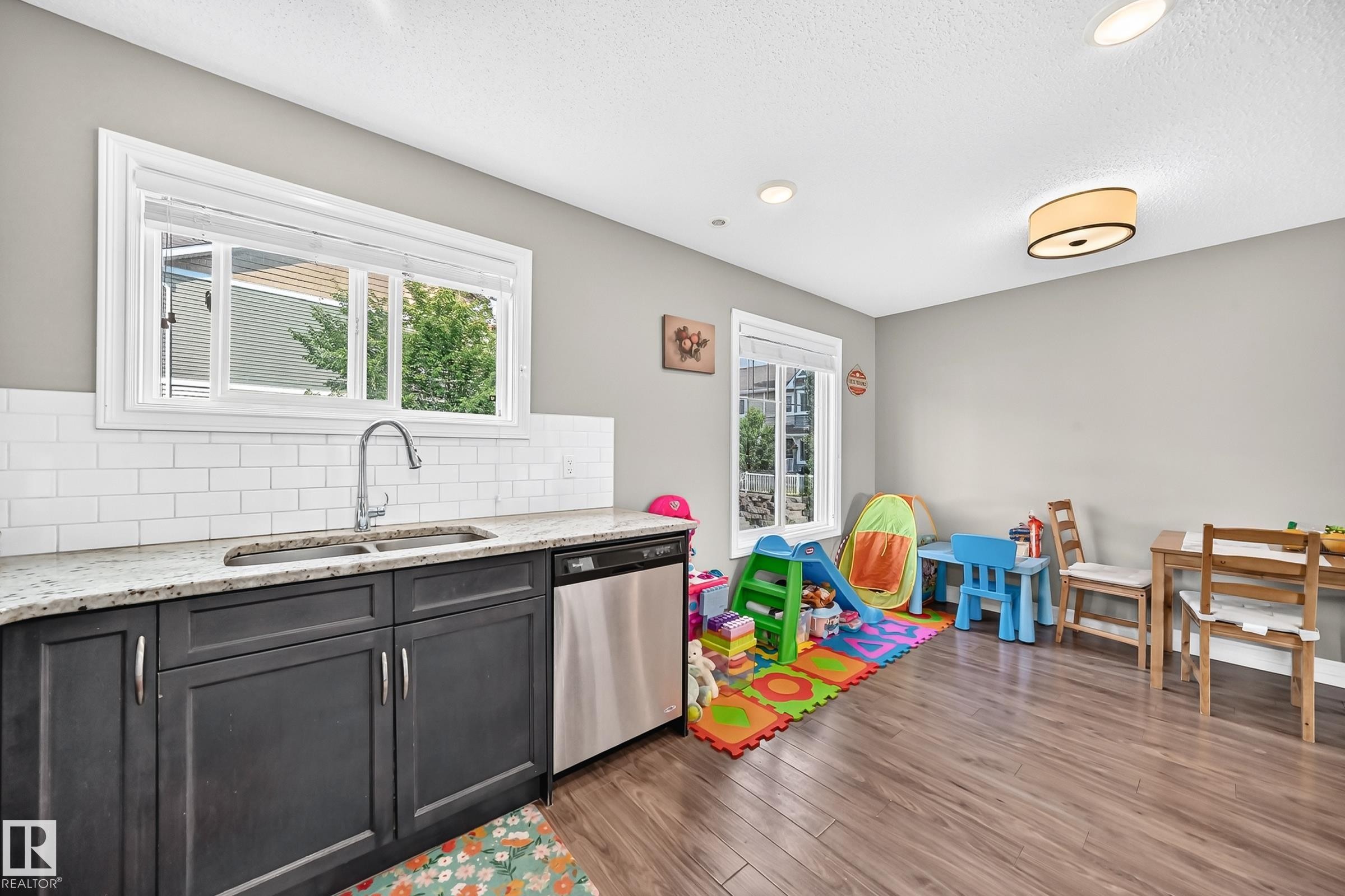 Kitchenette featuring dark-stained cabinetry, a stainless steel sink with a gooseneck faucet, light-toned granite countertops, and a subway tile backsplash - 415 Clareview Rd Nw Nw, Edmonton, AB - Indoor Photo Showing Kitchen With Double Sink