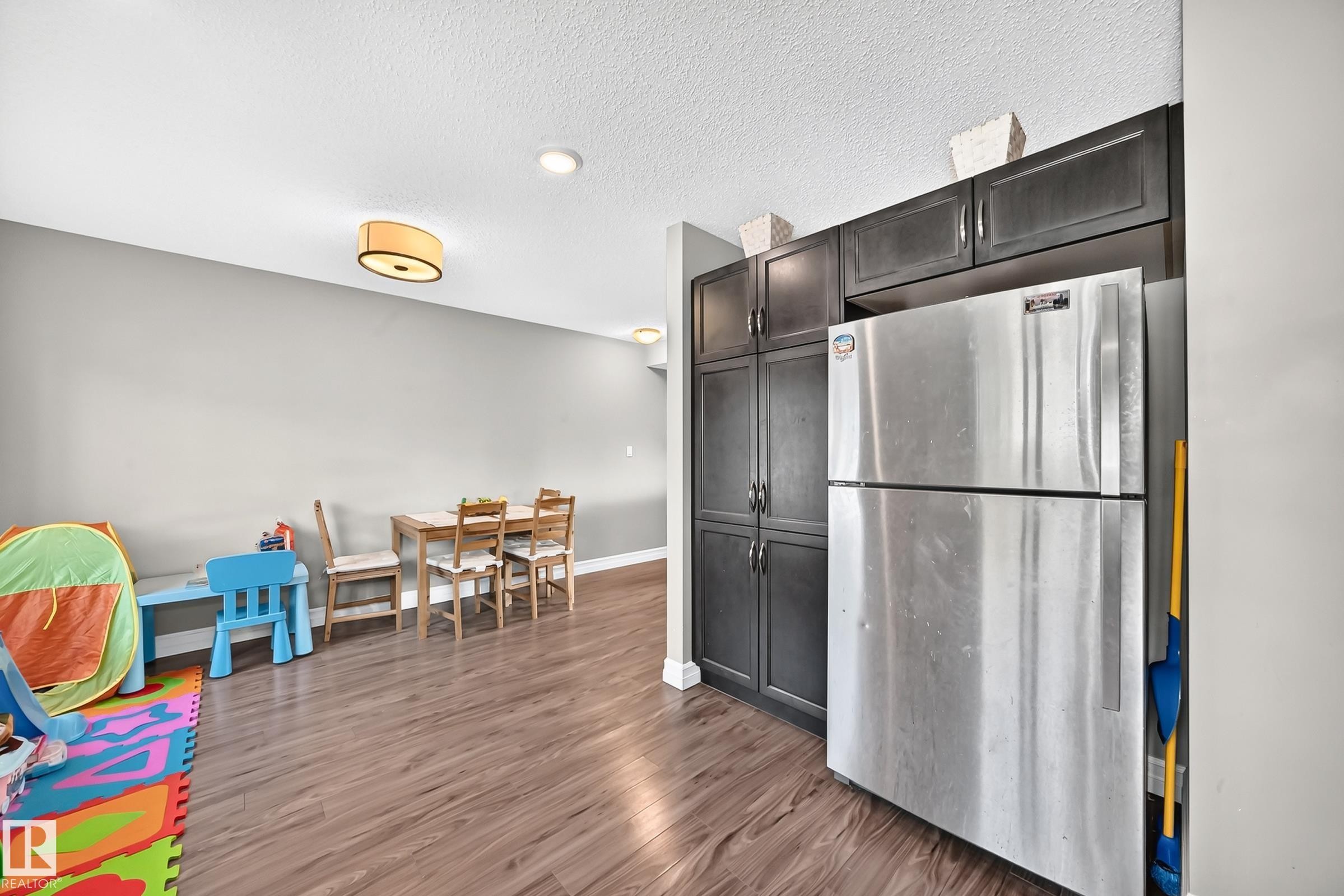 Integrated kitchen cabinetry with a stainless steel refrigerator, complemented by wood-finish flooring and light gray walls - 415 Clareview Rd Nw Nw, Edmonton, AB - Indoor