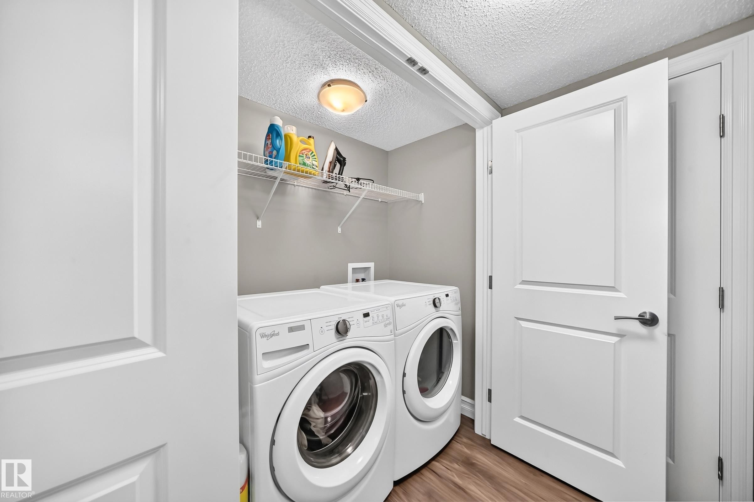 Dedicated laundry area featuring a washer and dryer, wood-finish flooring, a wire storage shelf, and a ceiling light fixture - 415 Clareview Rd Nw Nw, Edmonton, AB - Indoor Photo Showing Laundry Room