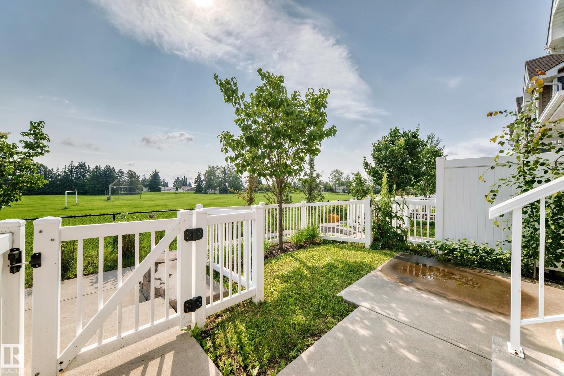 Private backyard featuring a white picket fence, concrete patio, and direct access to an expansive green field - 415 Clareview Rd Nw Nw, Edmonton, AB - Outdoor