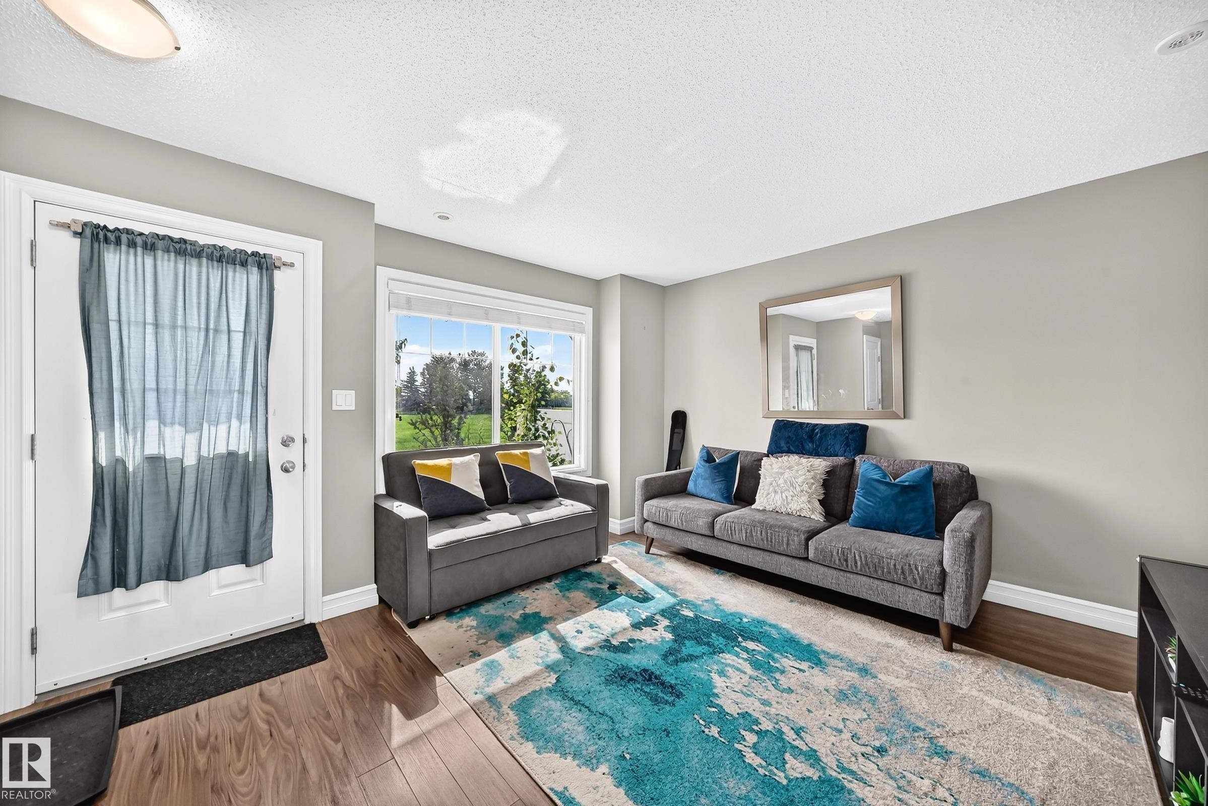 Living area featuring wood-finish flooring, neutral wall tones, and a large window providing ample natural light - 415 Clareview Rd Nw Nw, Edmonton, AB - Indoor Photo Showing Living Room