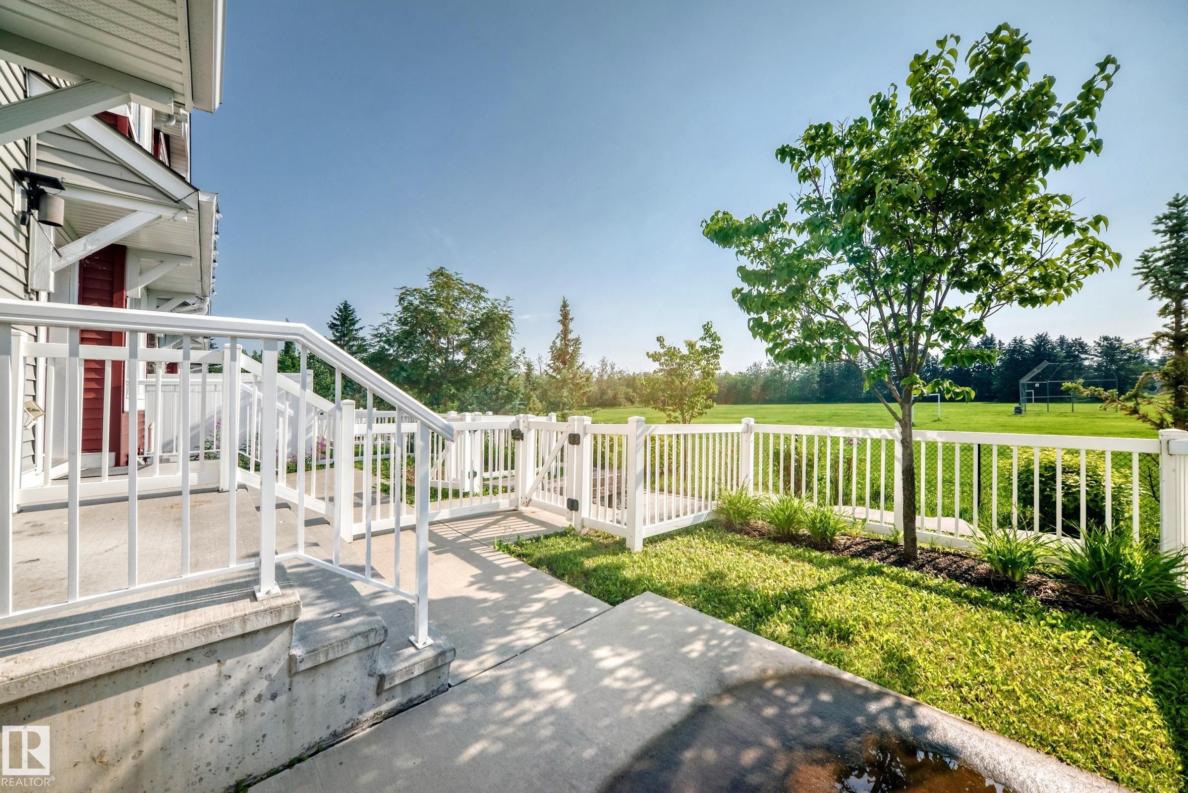 Outdoor concrete patio featuring white railings, a white picket fence, and a manicured lawn with a young tree - 415 Clareview Rd Nw Nw, Edmonton, AB - Outdoor