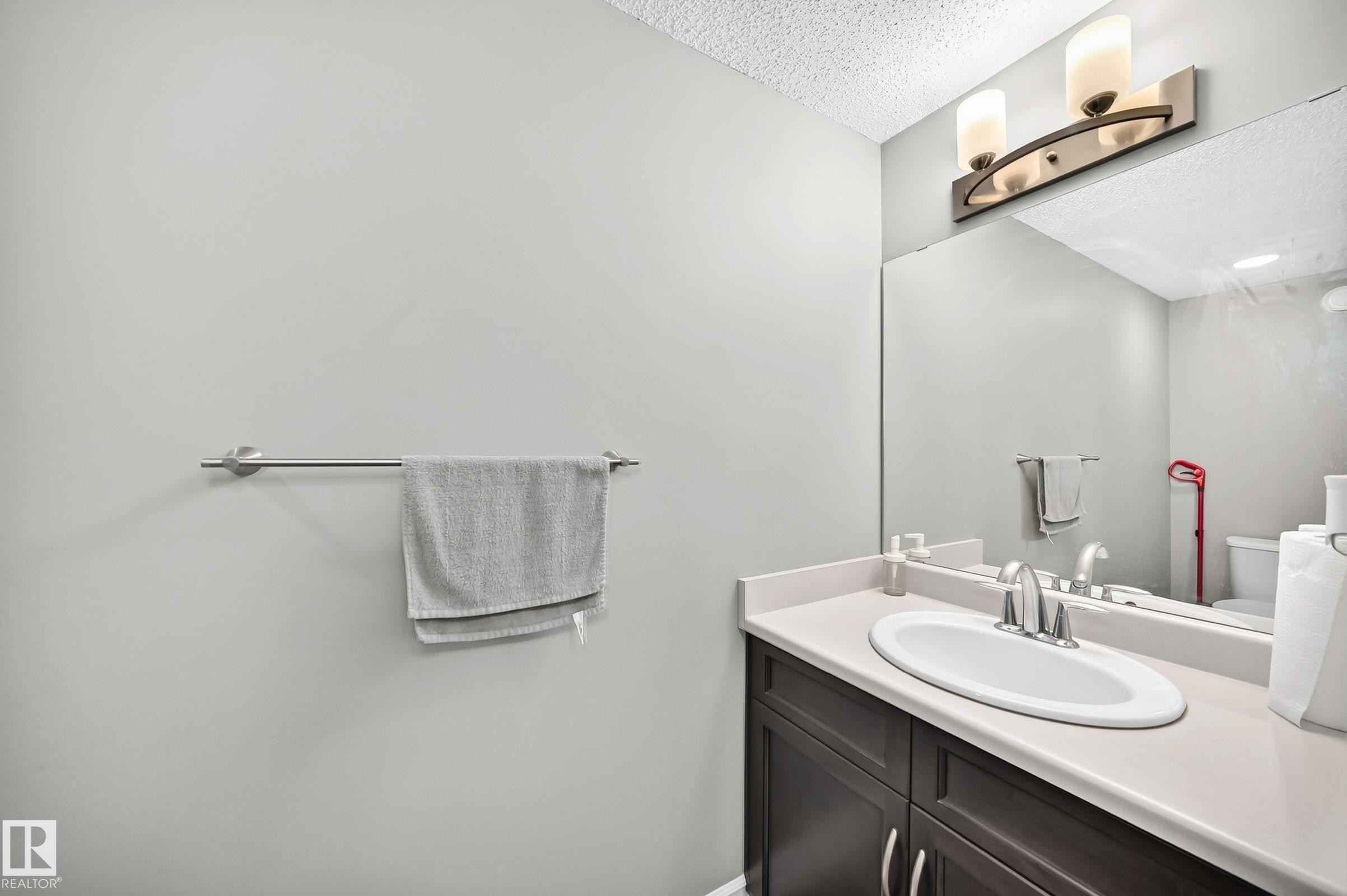 Bathroom vanity featuring a dark wood-finish cabinet with silver-tone hardware, a white oval undermount sink, and a light-toned countertop - 415 Clareview Rd Nw Nw, Edmonton, AB - Indoor Photo Showing Bathroom