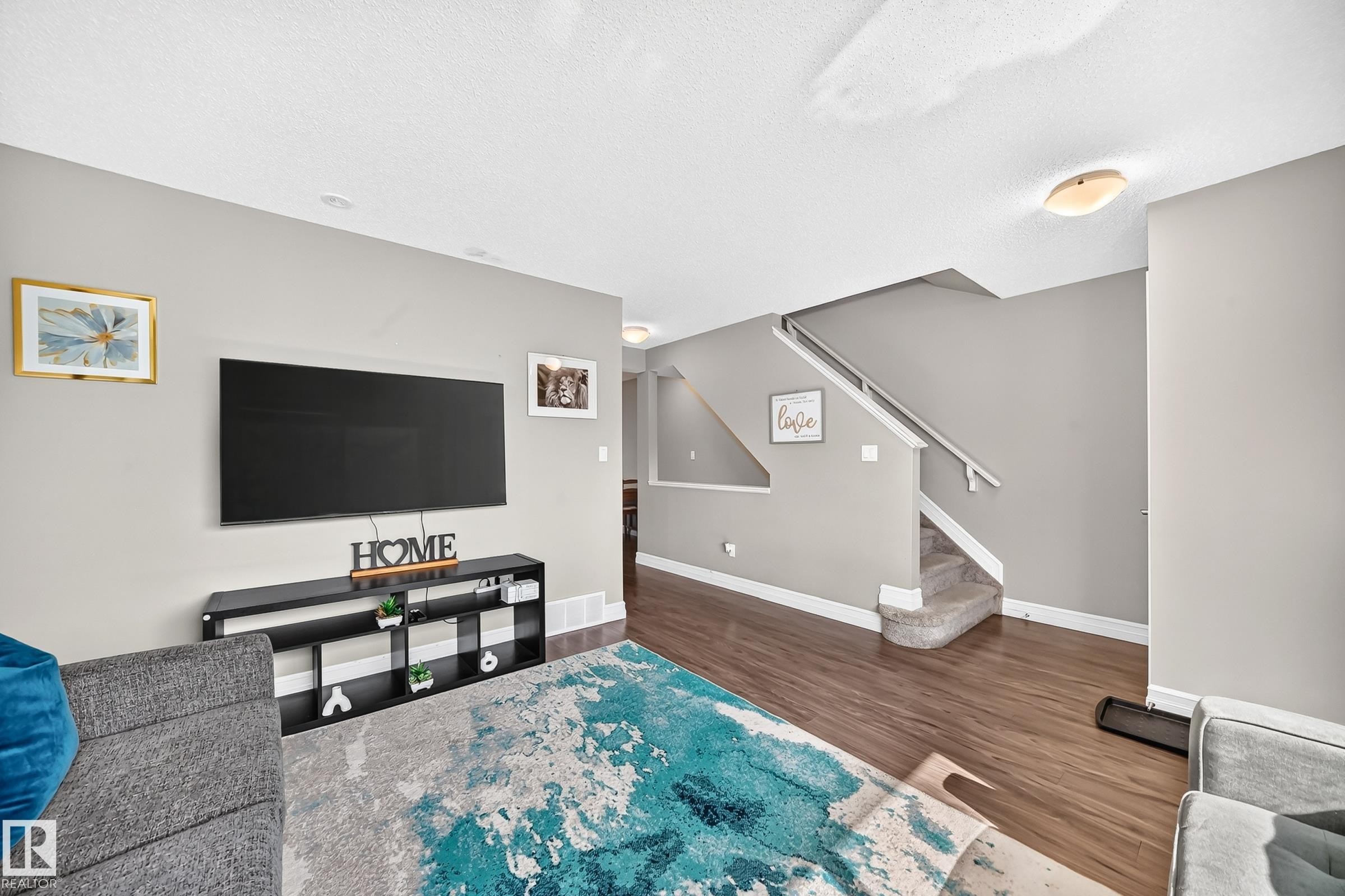 Open-concept living area featuring wood-finish flooring, a contemporary staircase with carpeted steps, and neutral painted walls - 415 Clareview Rd Nw Nw, Edmonton, AB - Indoor Photo Showing Other Room