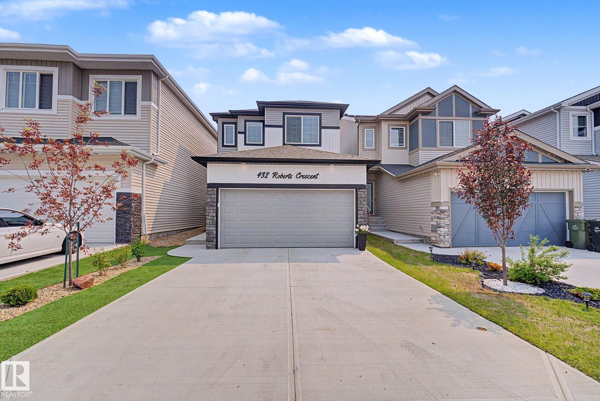 Modern two-story residence featuring a paved driveway, integrated garage, and stone facade accents - 432 Roberts Crescent, Leduc, AB