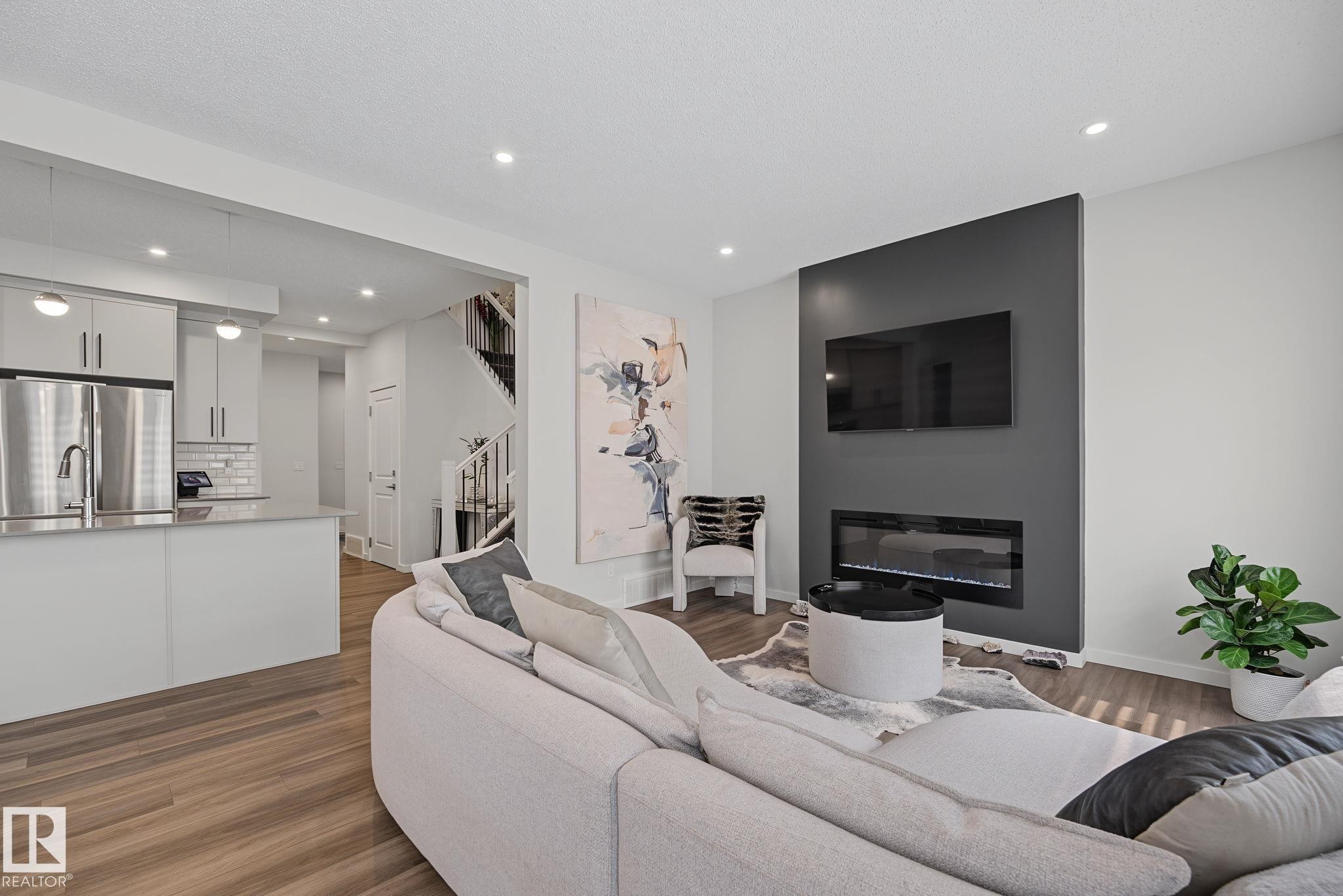 Open-concept living space featuring wood-finish flooring, recessed lighting, and a modern fireplace with a dark accent wall - 432 Roberts Crescent, Leduc, AB