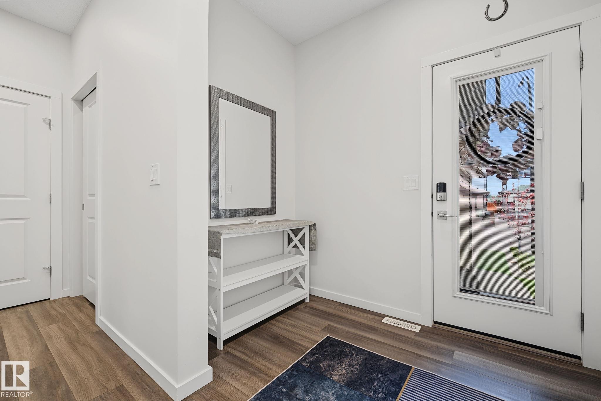 Entryway featuring wood-finish flooring, white baseboards, and a white interior door with a full-lite glass insert and a digital lock - 432 Roberts Crescent, Leduc, AB