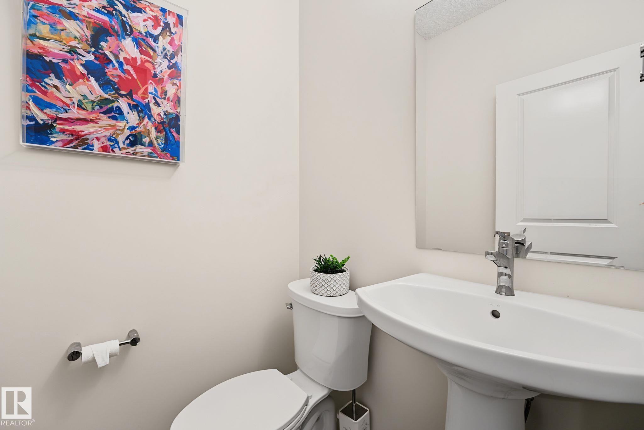 Pedestal sink with chrome faucet, toilet, and wall-mounted mirror - 432 Roberts Crescent, Leduc, AB