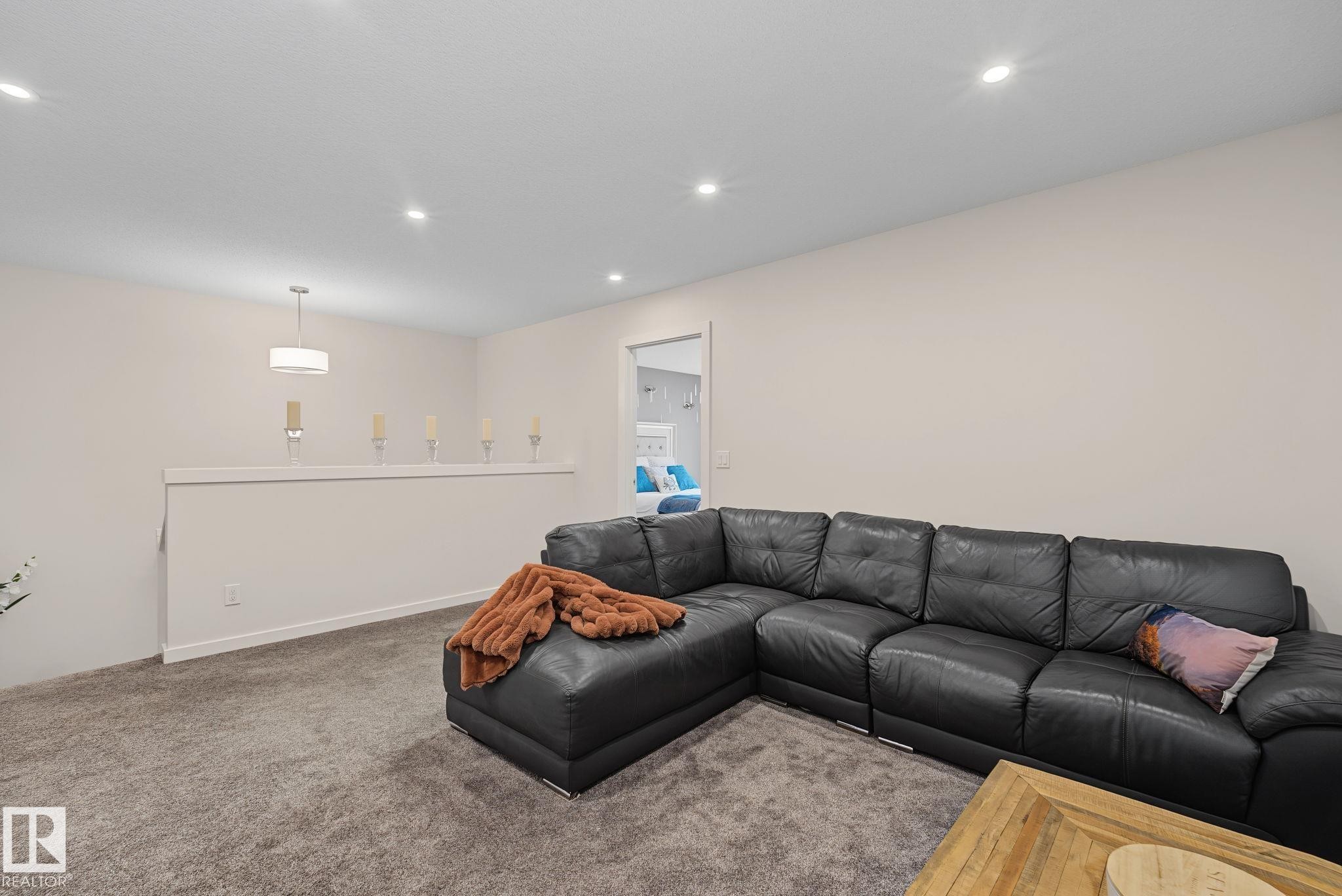 Carpeted entertainment area featuring recessed lighting, a neutral wall color, and a half-wall partition with a modern pendant light fixture - 432 Roberts Crescent, Leduc, AB