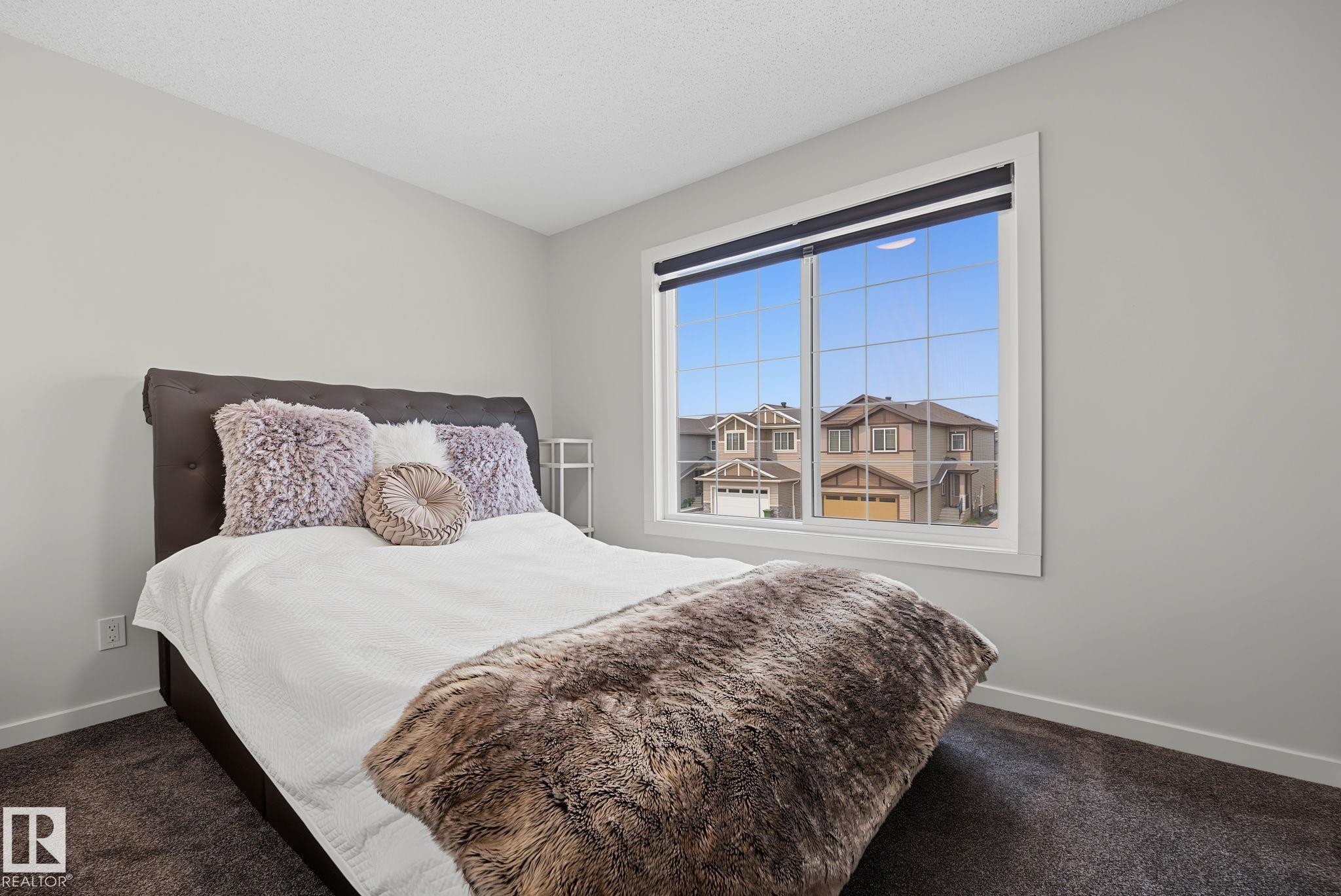 Carpeted bedroom featuring a large window with white trim, light gray walls, and a textured headboard - 432 Roberts Crescent, Leduc, AB