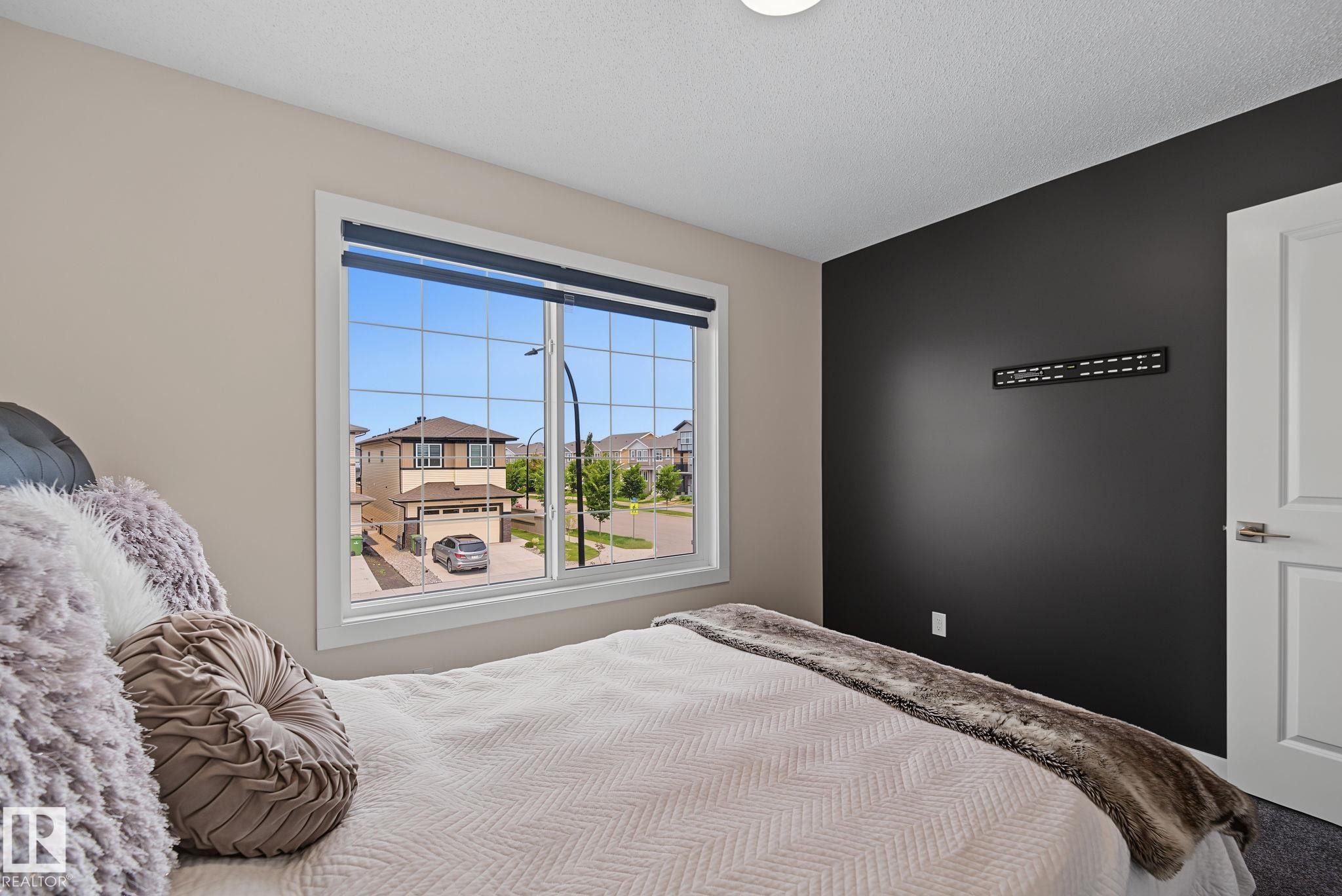 Bedroom featuring a large multi-pane window, dark accent wall, ceiling-mounted light fixture, and white interior door with brushed nickel hardware - 432 Roberts Crescent, Leduc, AB