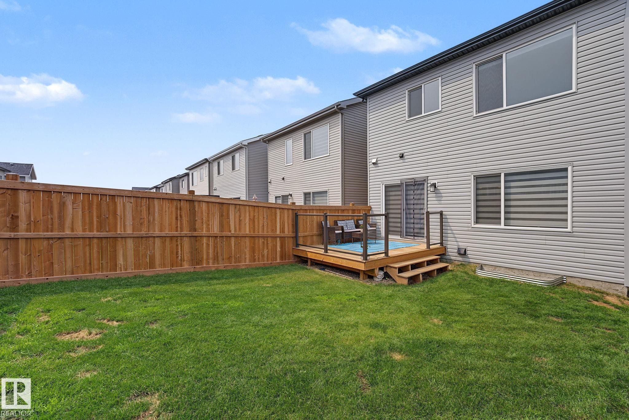 Expansive fenced backyard featuring a wooden deck with glass panel railings and a two-step entry - 432 Roberts Crescent, Leduc, AB