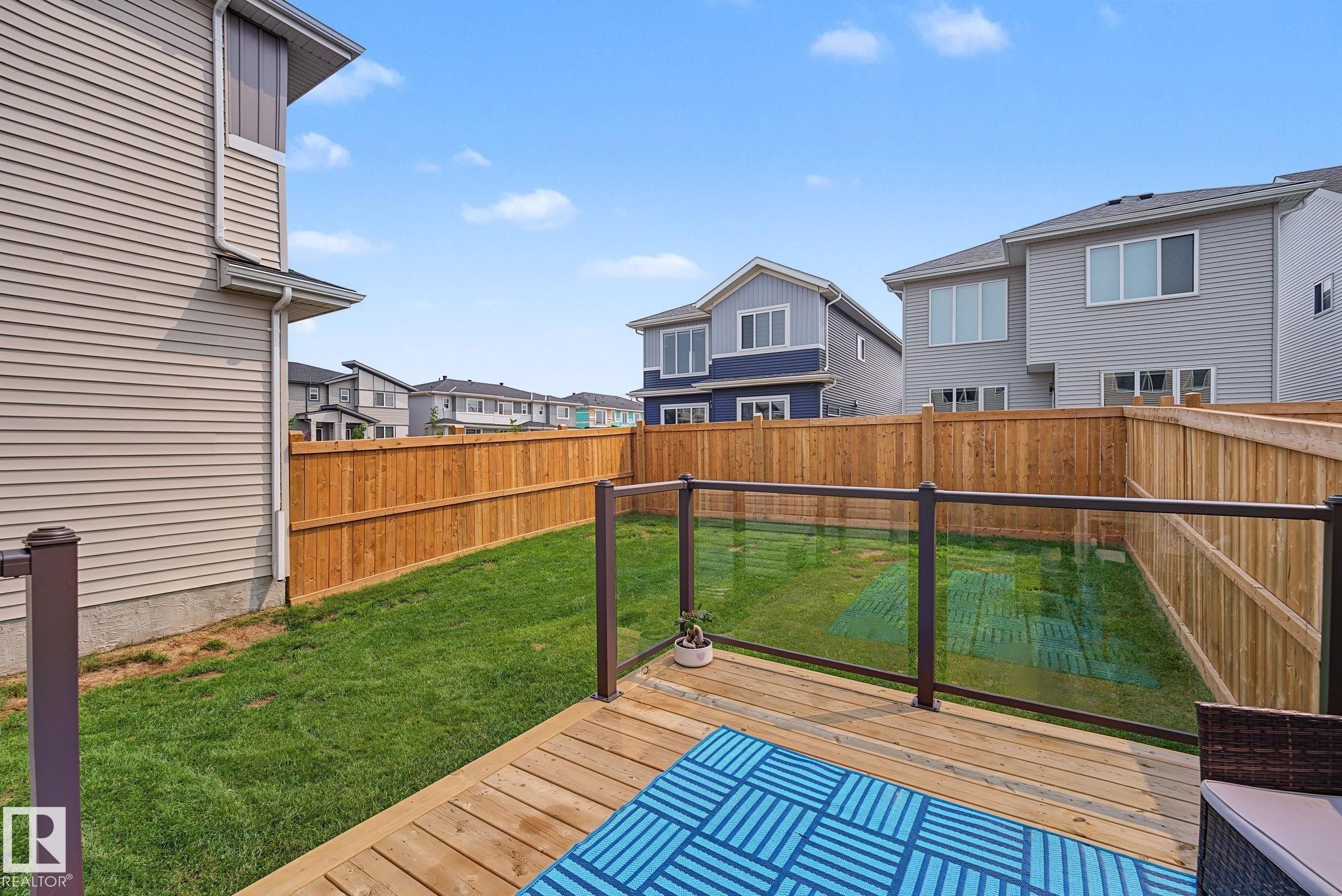 Expansive backyard featuring a natural wood deck with glass panel railings, a manicured lawn, and a perimeter wood fence - 432 Roberts Crescent, Leduc, AB