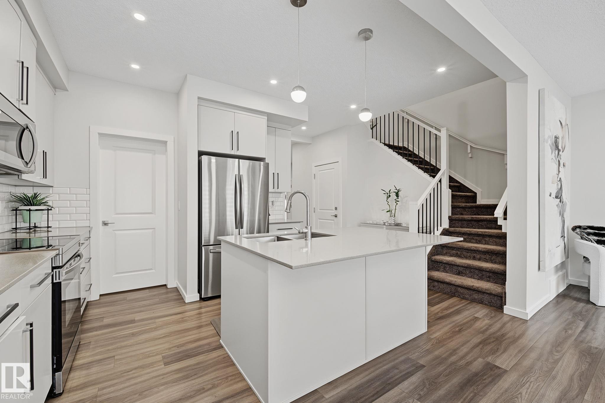 Contemporary kitchen featuring a center island with sink, stainless steel appliances, white subway tile backsplash, and wood-finish flooring - 432 Roberts Crescent, Leduc, AB