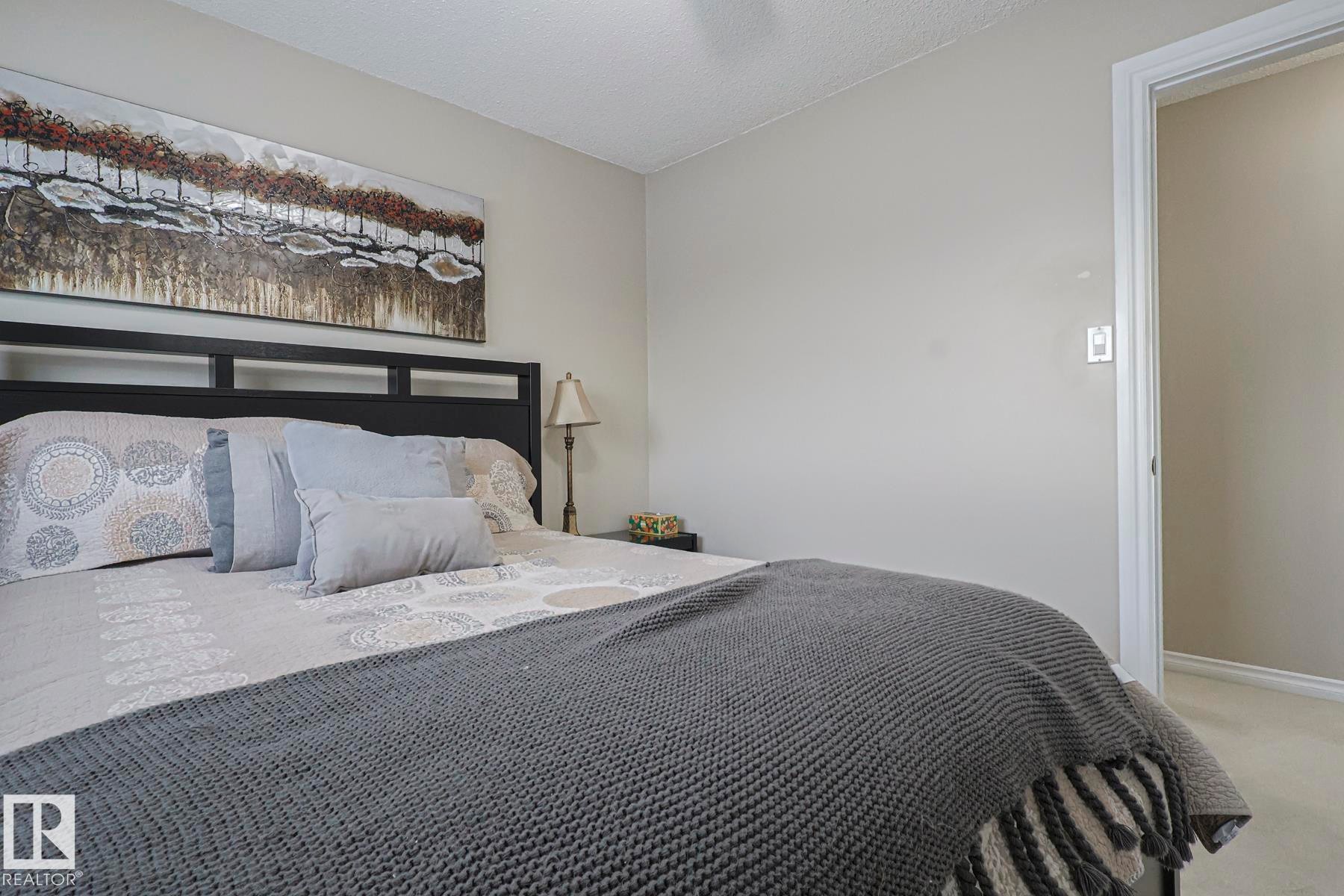 Bedroom featuring a dark-finish bed frame, light-toned walls, and a textured ceiling - 13304 70 Street, Edmonton, AB