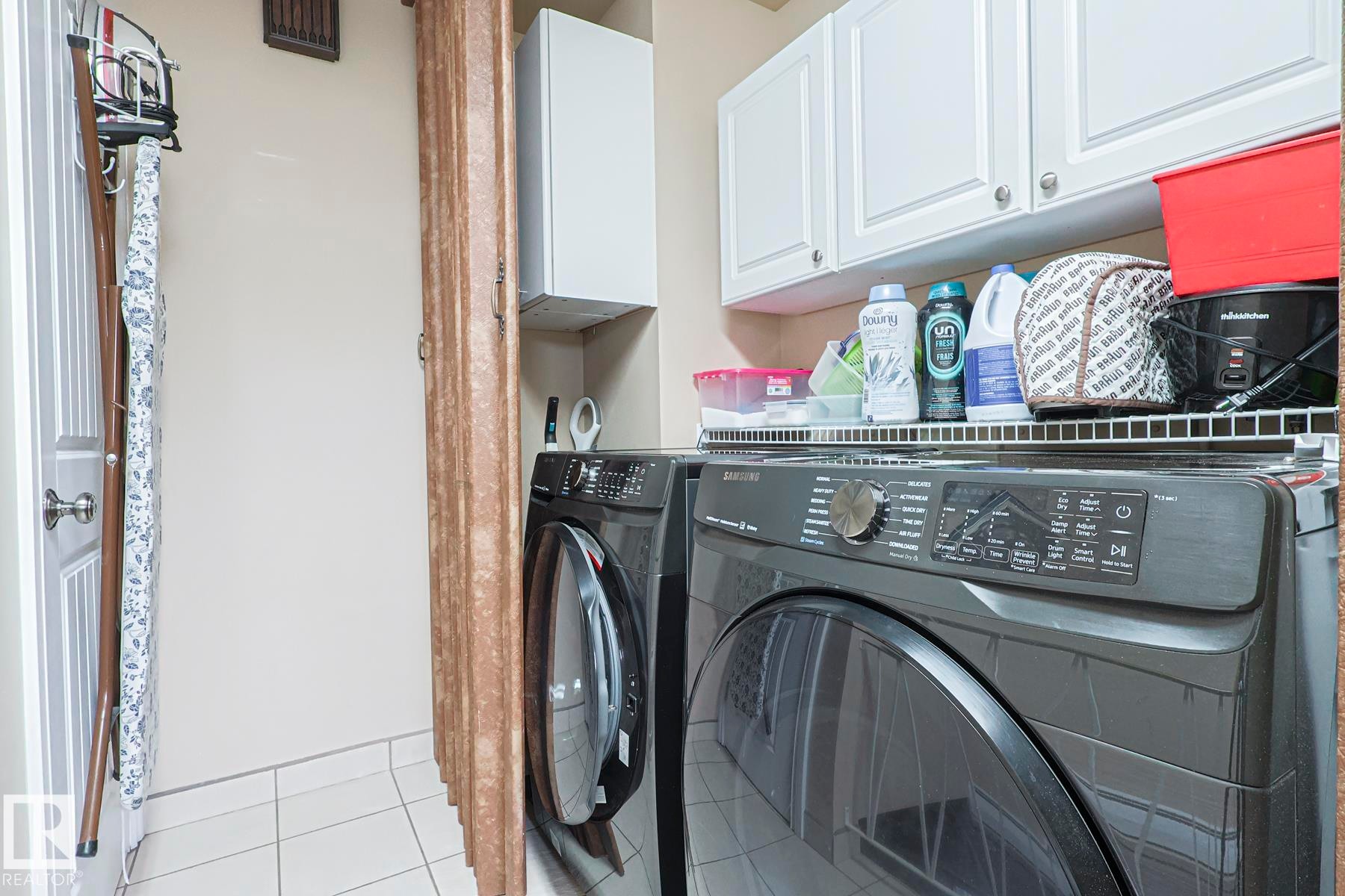 Dedicated laundry area featuring tile flooring, white shaker-style cabinetry, and a built-in wire shelf - 13304 70 Street, Edmonton, AB
