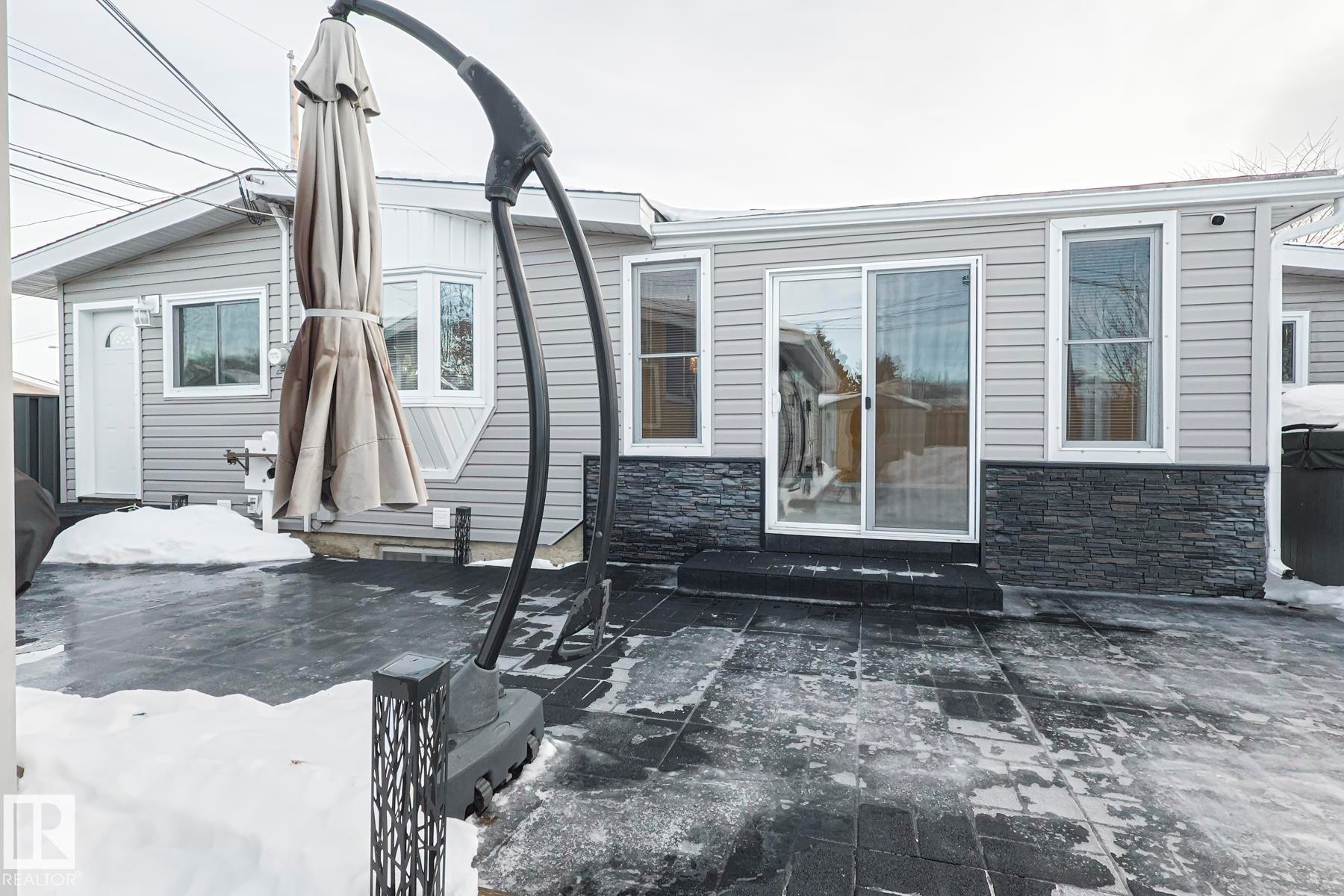 Rear exterior featuring gray siding with a dark stone veneer accent - 13304 70 Street, Edmonton, AB