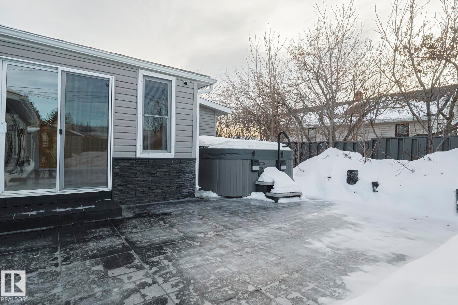 Exterior patio with a built-in hot tub, grey horizontal siding, and a dark stone veneer foundation - 13304 70 Street, Edmonton, AB