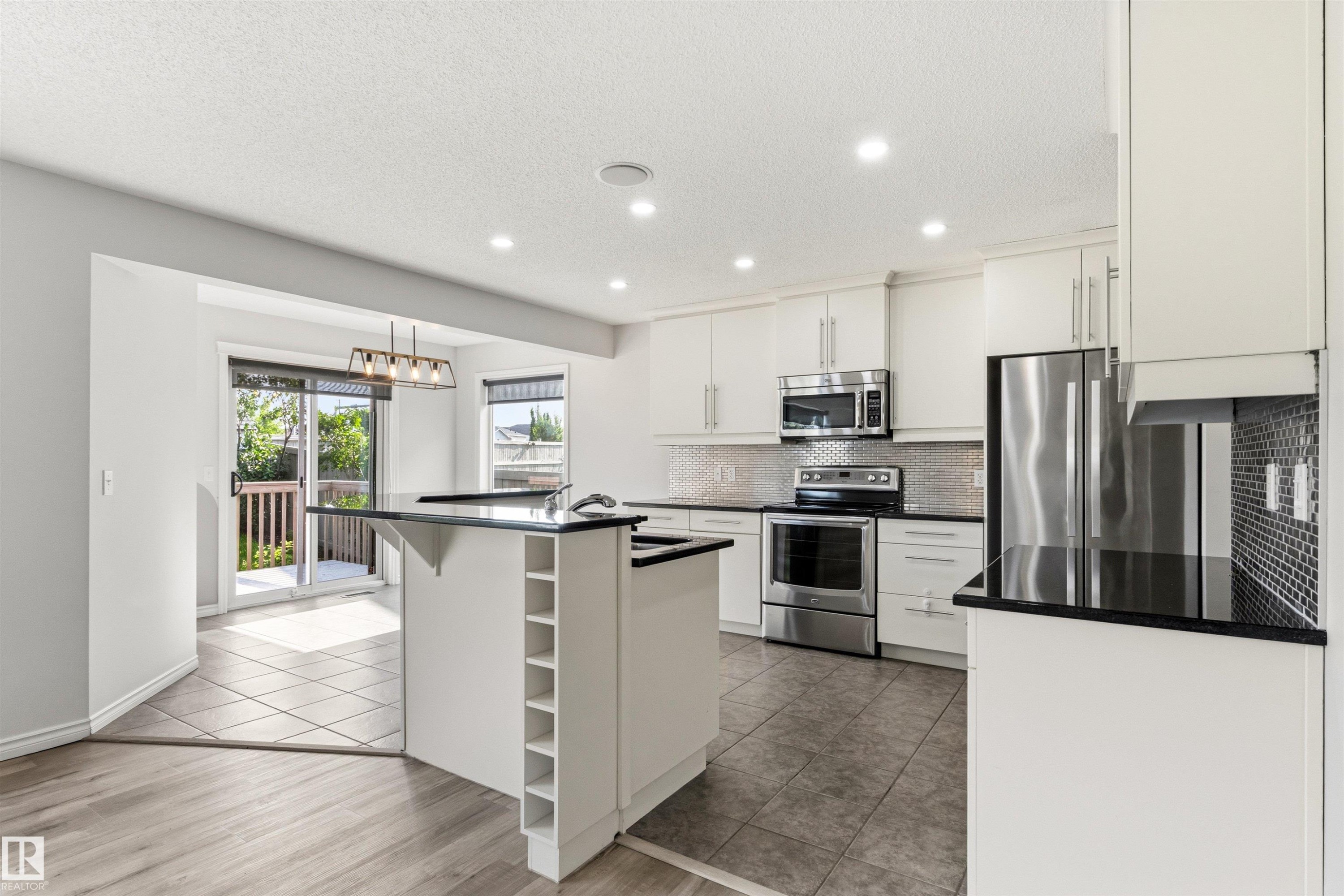 Modern kitchen featuring white cabinetry, stainless steel appliances, black countertops, and a tile backsplash - 3214 22A Avenue Nw, Edmonton, AB - Indoor Photo Showing Kitchen With Stainless Steel Kitchen With Upgraded Kitchen