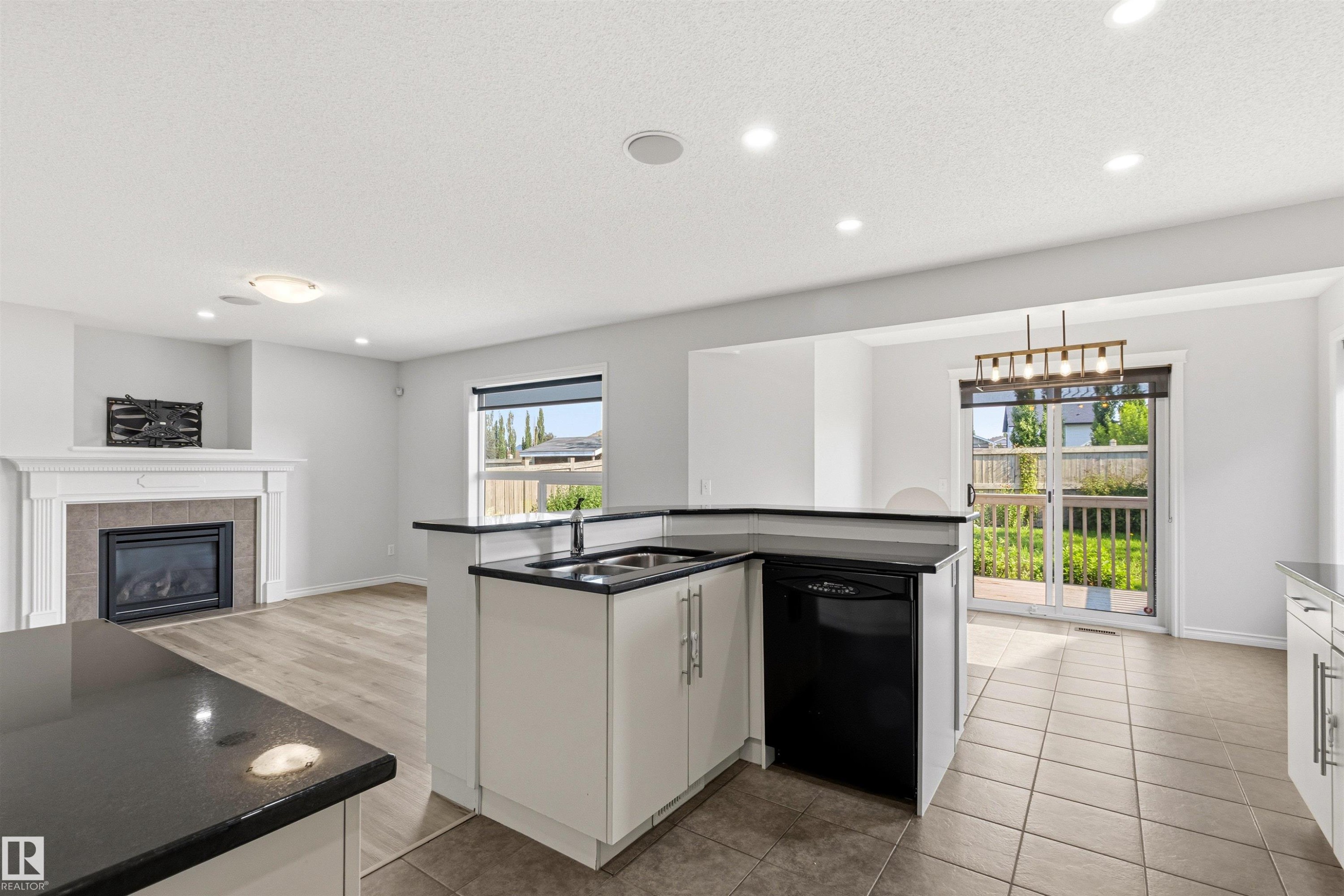 Open-concept living area featuring a kitchen island with black countertops and an integrated sink - 3214 22A Avenue Nw, Edmonton, AB - Indoor With Fireplace