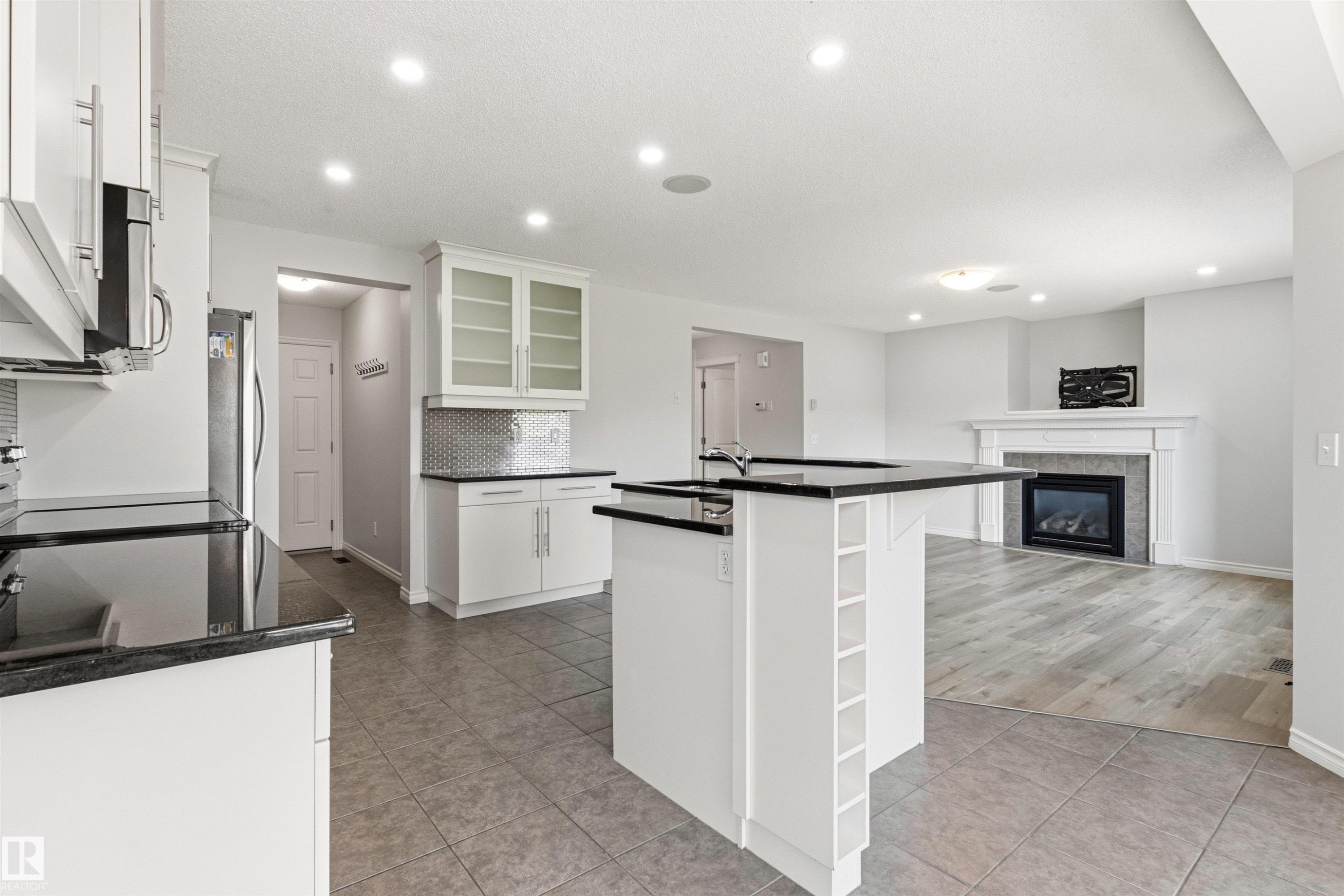 Open-concept kitchen and living area featuring white cabinetry, dark countertops, a kitchen island with built-in storage, and recessed lighting - 3214 22A Avenue Nw, Edmonton, AB - Indoor Photo Showing Kitchen
