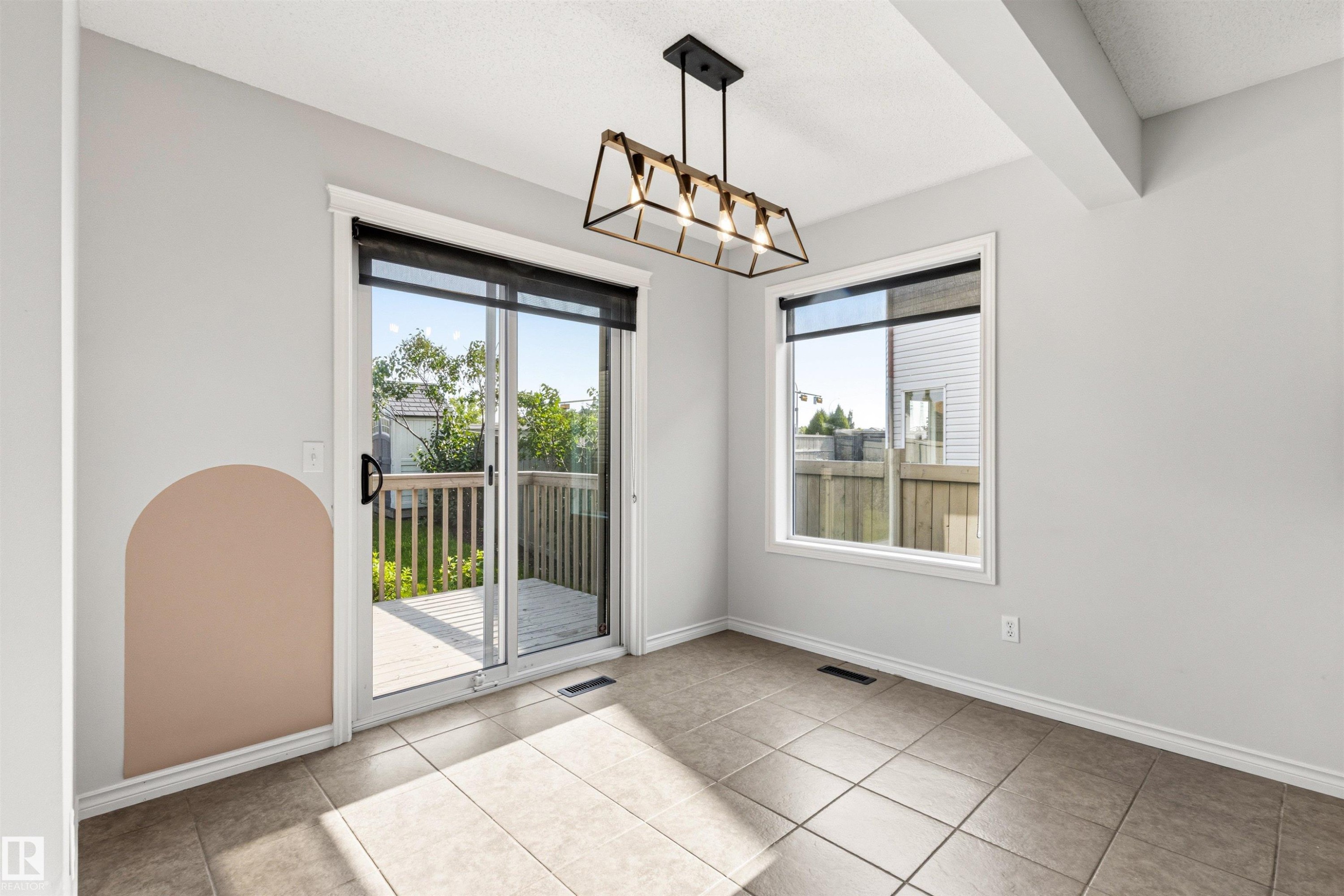 Ceramic tile flooring, a sliding glass door leading to a wooden deck, a rectangular window, and a linear pendant light fixture - 3214 22A Avenue Nw, Edmonton, AB - Indoor Photo Showing Other Room