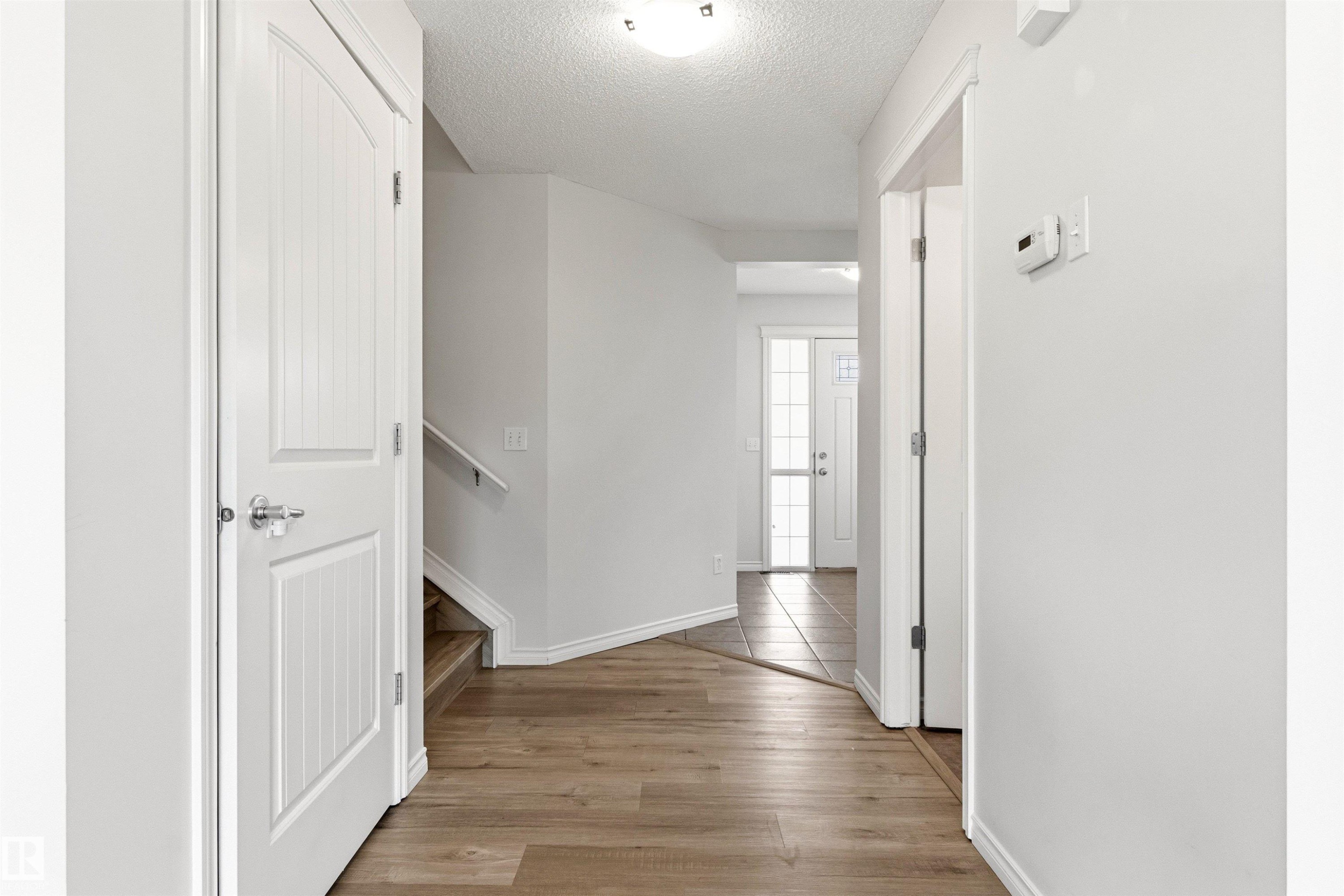 Neutral-toned hallway featuring wood-finish flooring, white trim, and a white interior door with polished hardware - 3214 22A Avenue Nw, Edmonton, AB - Indoor Photo Showing Other Room