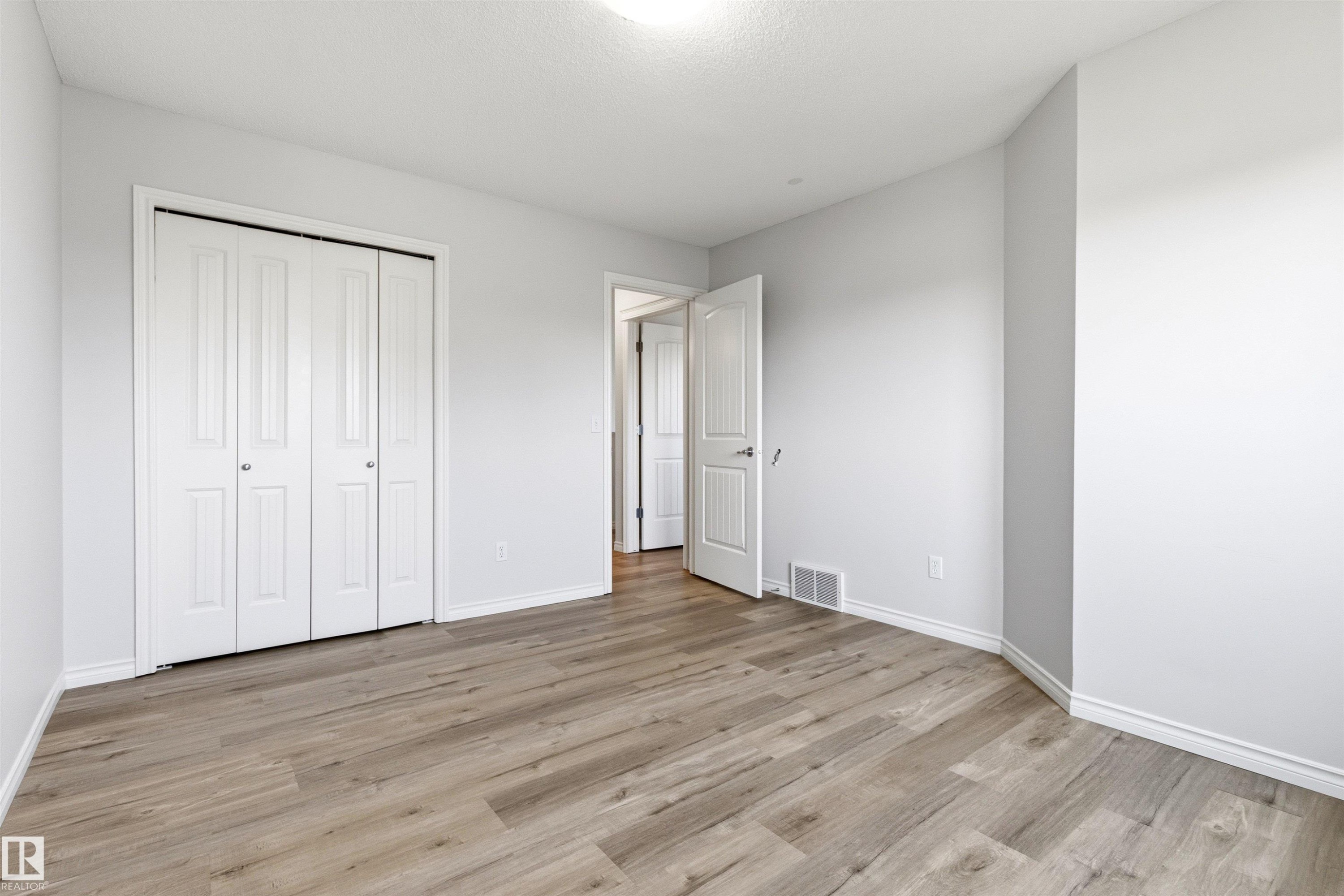 Room featuring light gray walls, wood-finish flooring, white trim, and a white bi-fold closet door - 3214 22A Avenue Nw, Edmonton, AB - Indoor Photo Showing Other Room