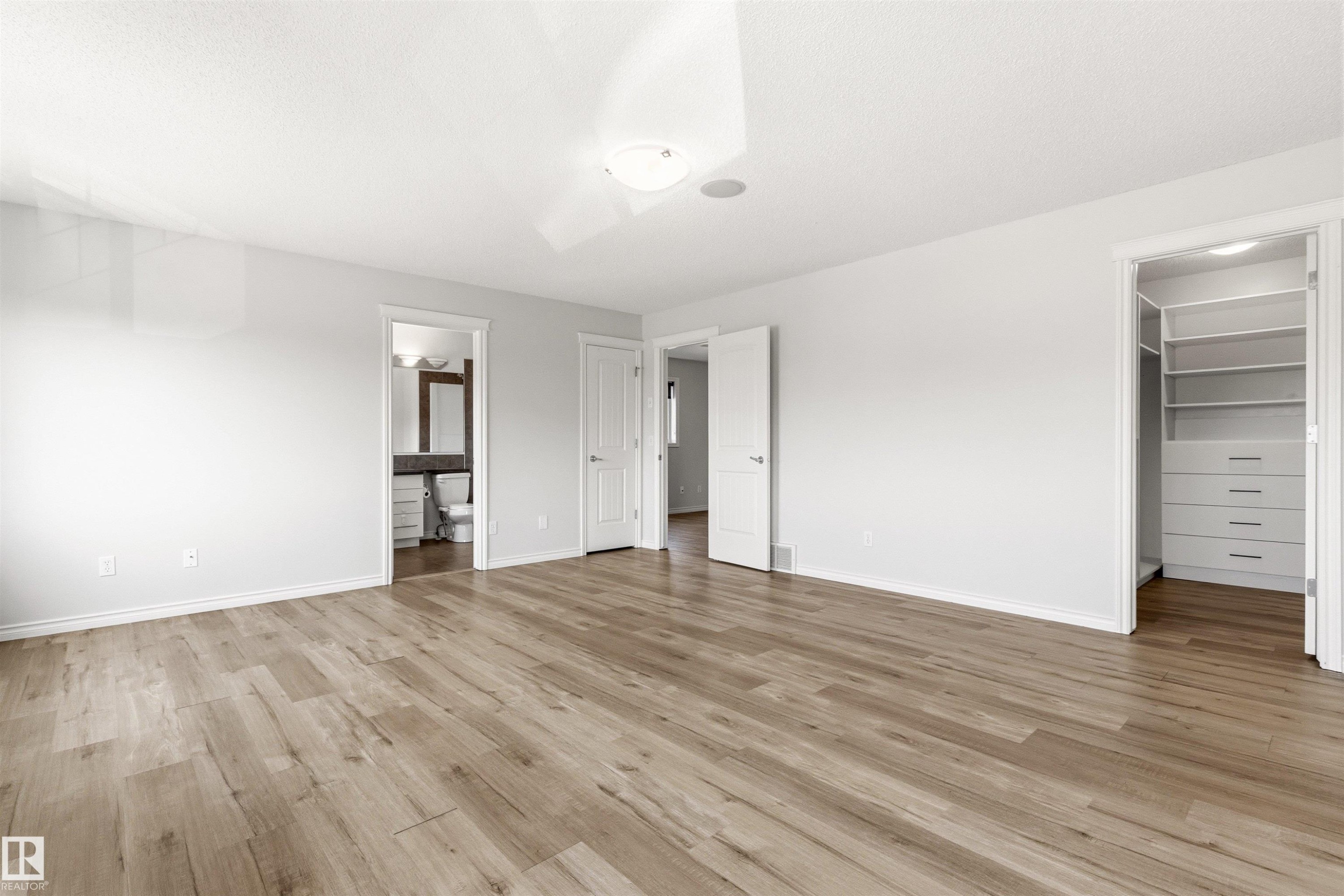 Spacious room featuring wood-finish flooring, a built-in closet system with shelving and drawers, a flush-mount ceiling light, and an integrated ceiling speaker - 3214 22A Avenue Nw, Edmonton, AB - Indoor Photo Showing Other Room