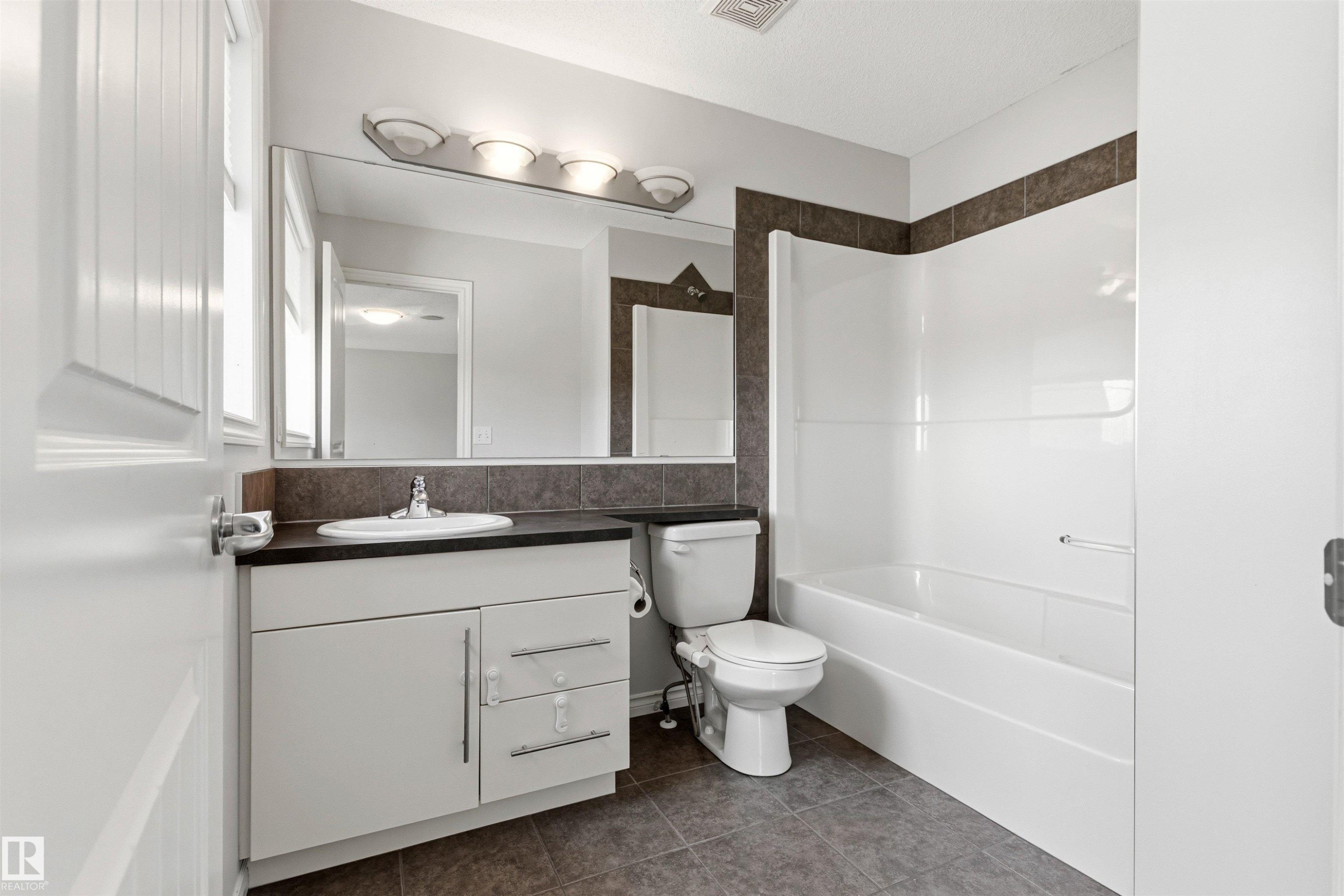 Full bathroom featuring a white vanity with integrated sink, dark countertop, and tiled backsplash - 3214 22A Avenue Nw, Edmonton, AB - Indoor Photo Showing Bathroom