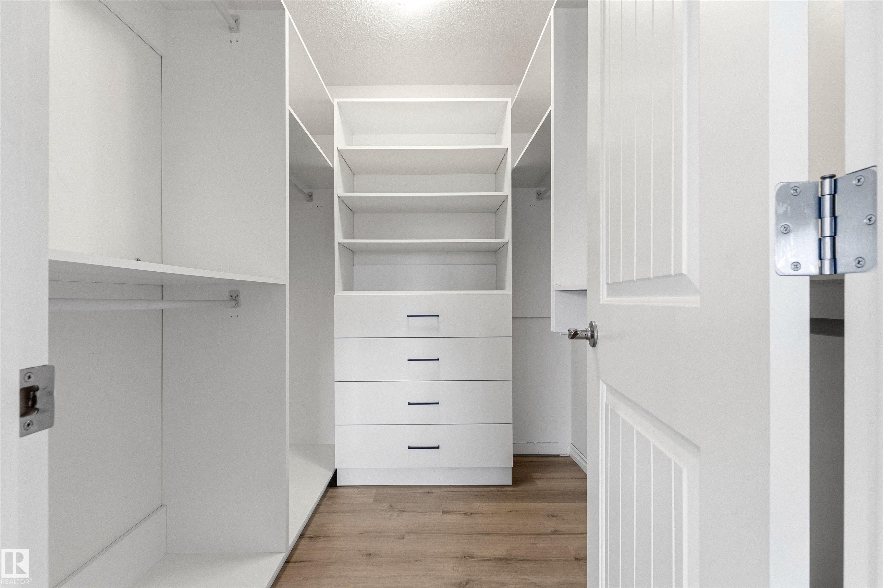 Walk-in closet with integrated shelving, multiple hanging rods, four built-in drawers with modern pulls, recessed lighting, and wood-finish flooring - 3214 22A Avenue Nw, Edmonton, AB - Indoor