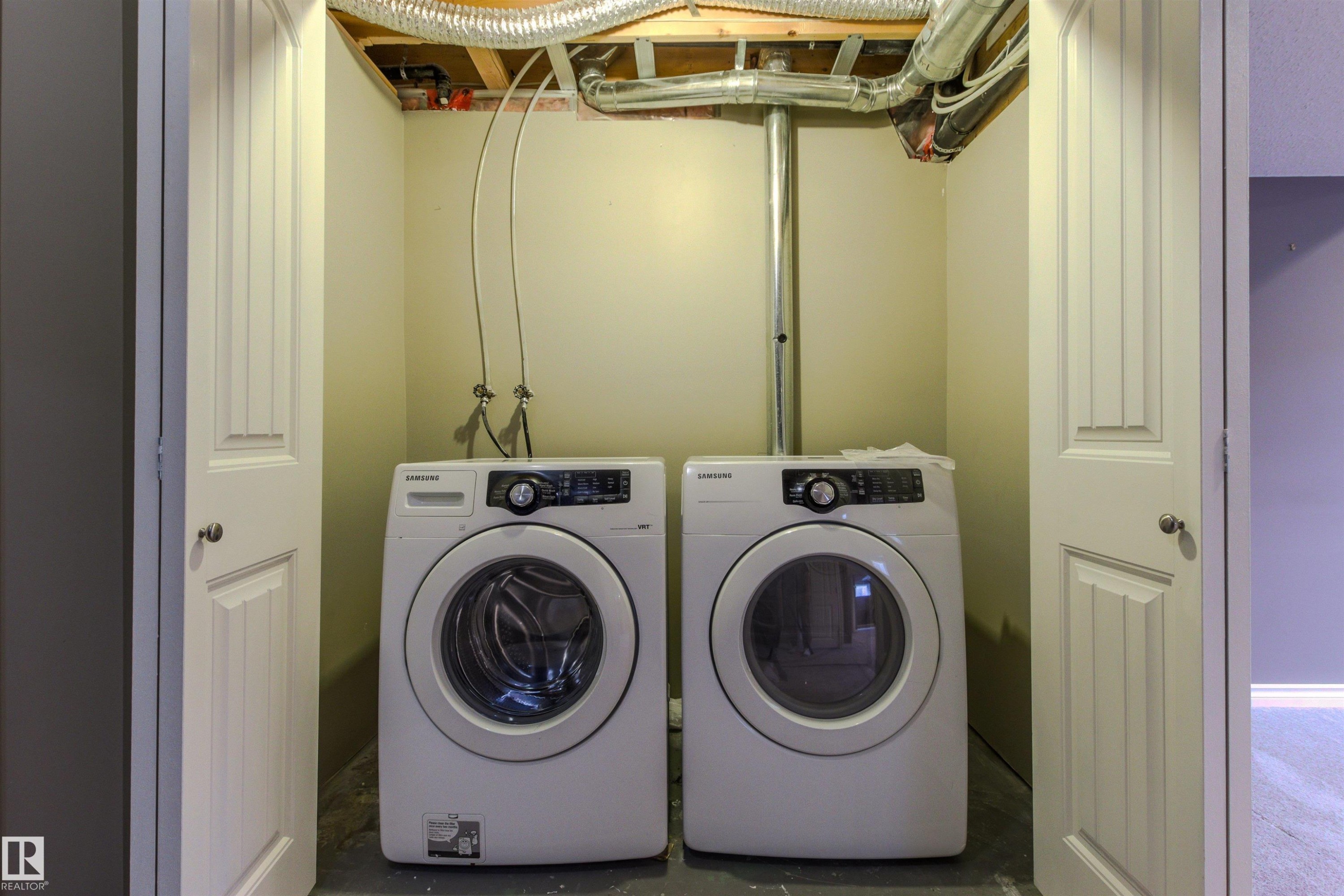 Dedicated laundry alcove featuring a front-loading washer and dryer, finished with neutral-toned walls and a concrete floor - 3214 22A Avenue Nw, Edmonton, AB - Indoor Photo Showing Laundry Room