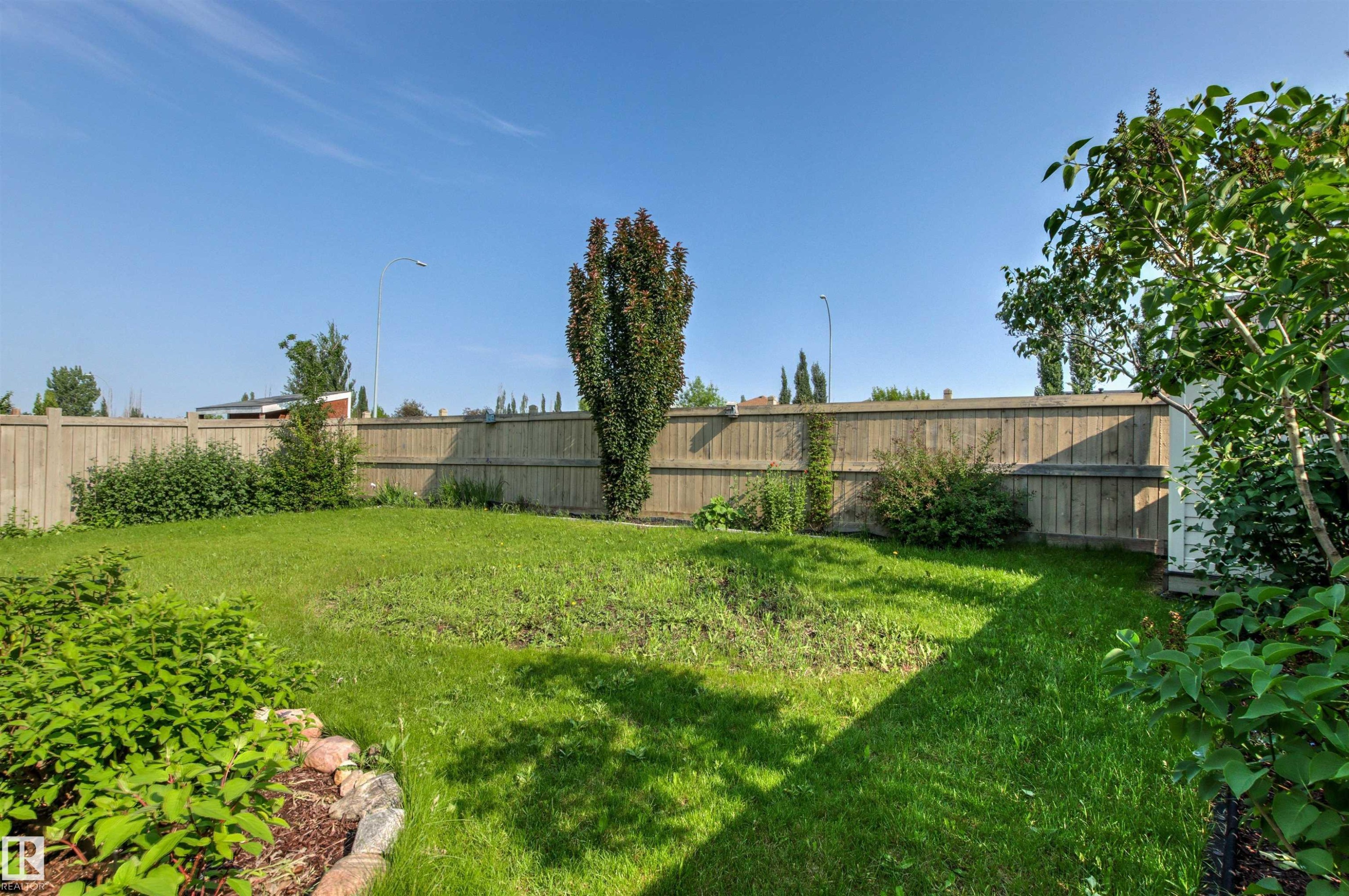Private backyard featuring a wooden privacy fence, established trees, and a landscaped garden bed with rock border - 3214 22A Avenue Nw, Edmonton, AB - Outdoor With Backyard