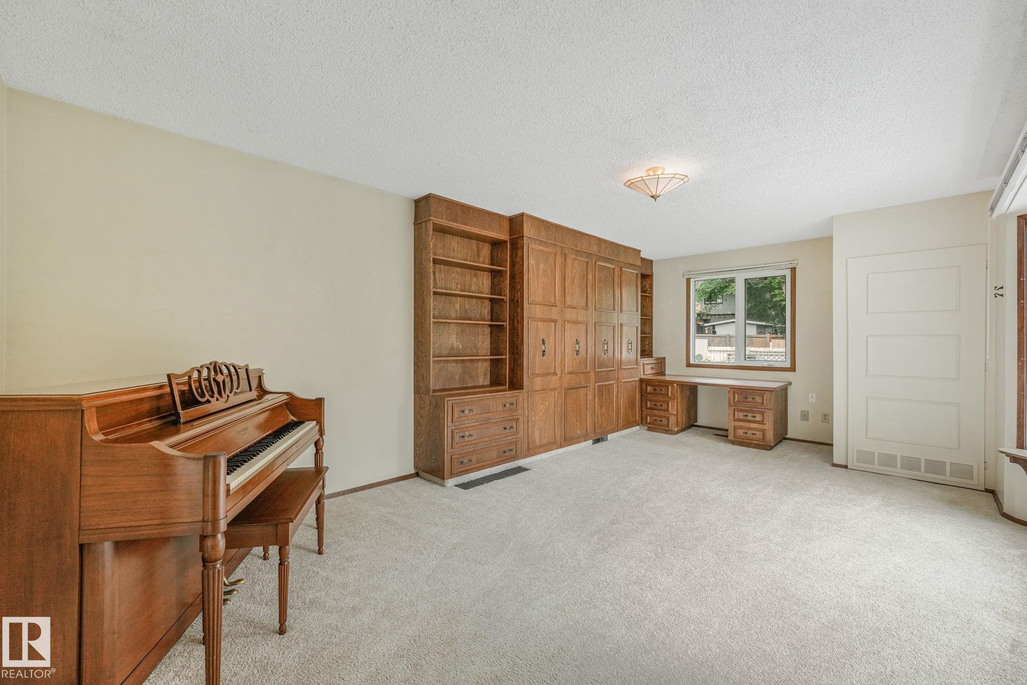 Spacious room featuring light-colored carpeting, a window with exterior views, and a large built-in wood-finish shelving and cabinet unit - 13320 79 Avenue Nw, Edmonton, AB - Indoor Photo Showing Other Room
