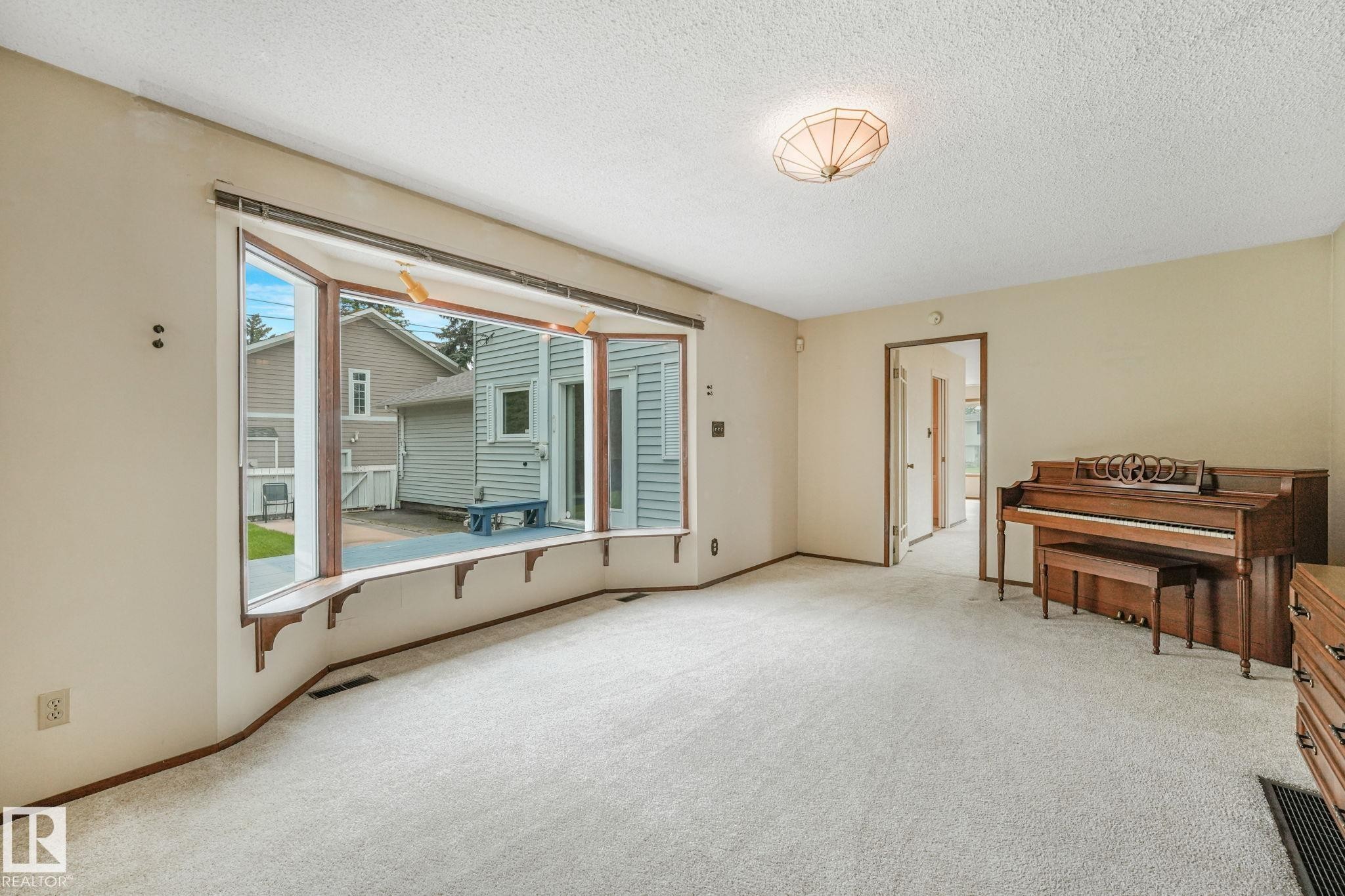 Spacious living area featuring a large bay window with wood trim, light-toned carpeting, and a textured ceiling - 13320 79 Avenue Nw, Edmonton, AB - Indoor Photo Showing Other Room