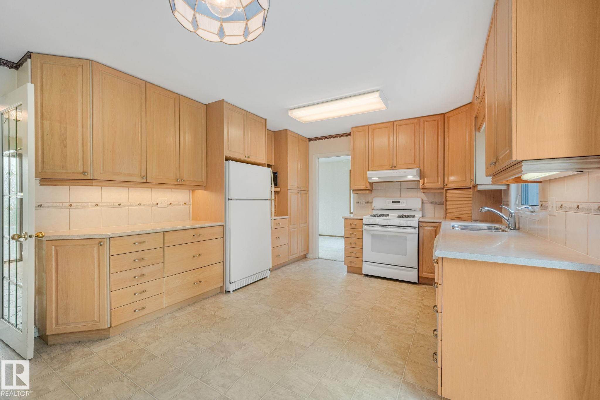 Kitchen featuring light wood cabinetry, white appliances, a tile backsplash, and light-toned flooring - 13320 79 Avenue Nw, Edmonton, AB - Indoor Photo Showing Kitchen