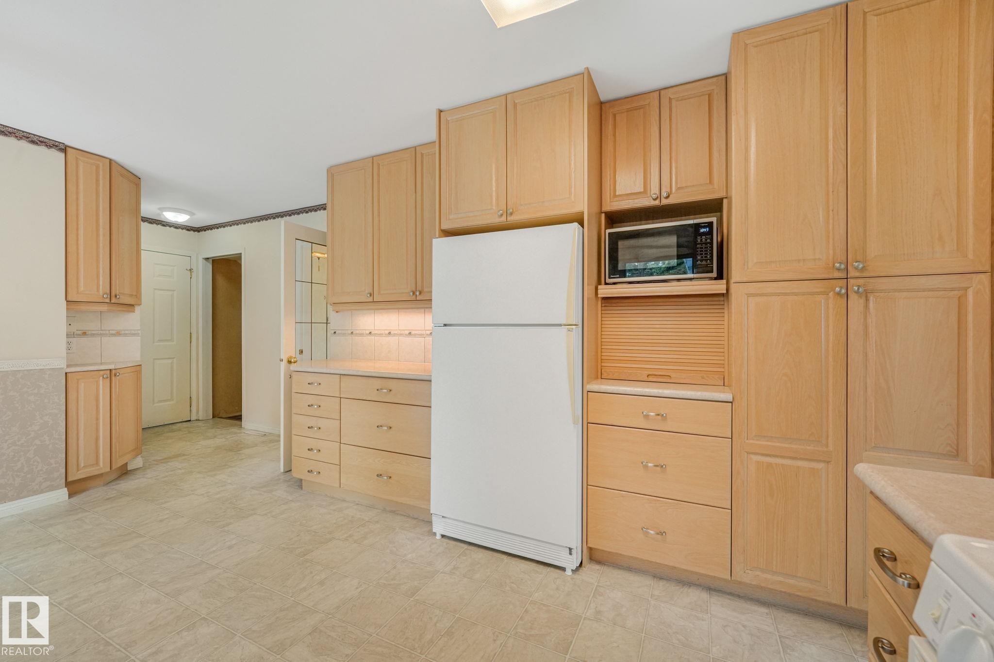Kitchen featuring light wood cabinetry, a built-in microwave, ample storage, light-toned countertops, and neutral tile flooring - 13320 79 Avenue Nw, Edmonton, AB - Indoor Photo Showing Kitchen