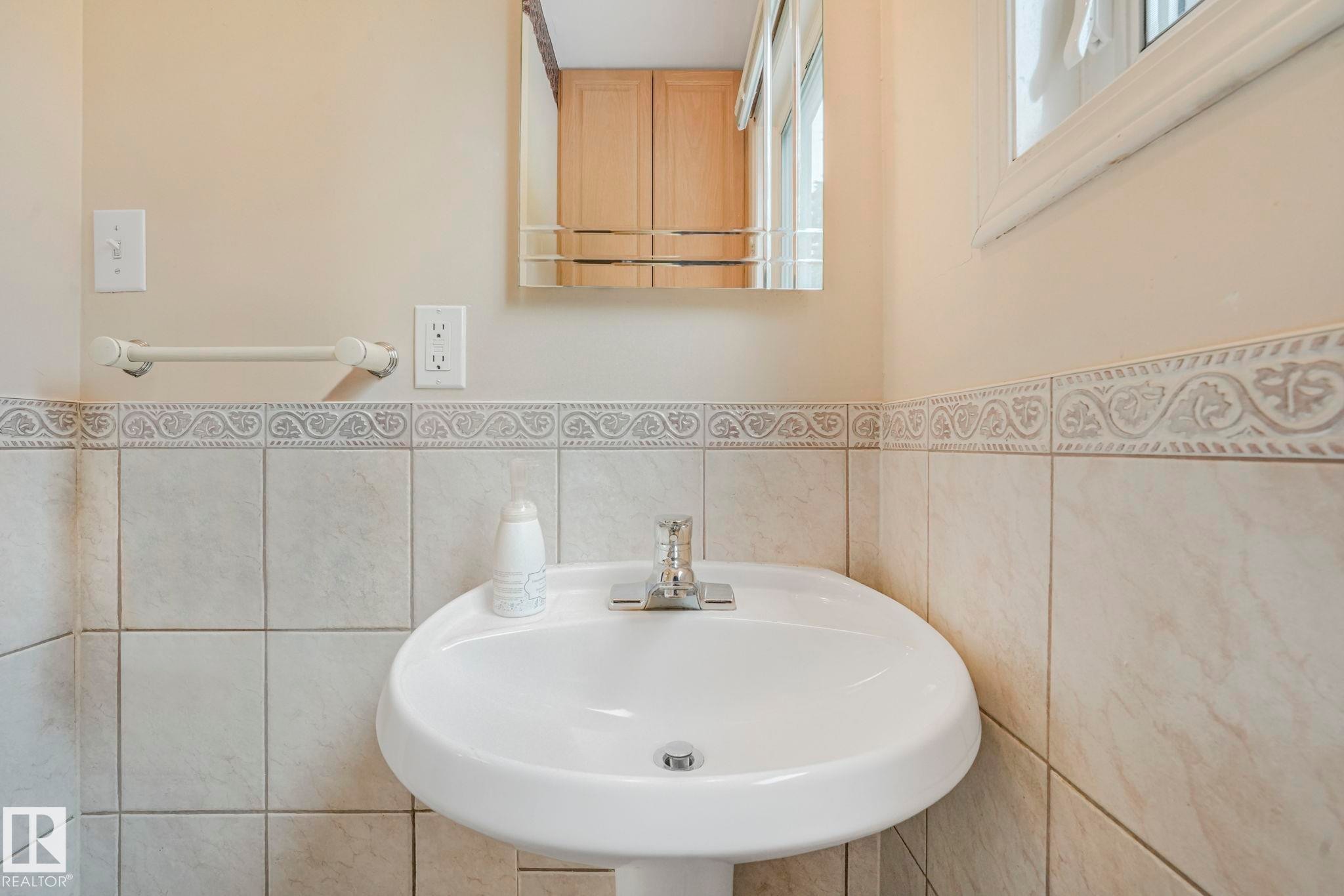 Pedestal sink with chrome faucet, light-toned wall tile, decorative tile border, and a framed window - 13320 79 Avenue Nw, Edmonton, AB - Indoor Photo Showing Bathroom
