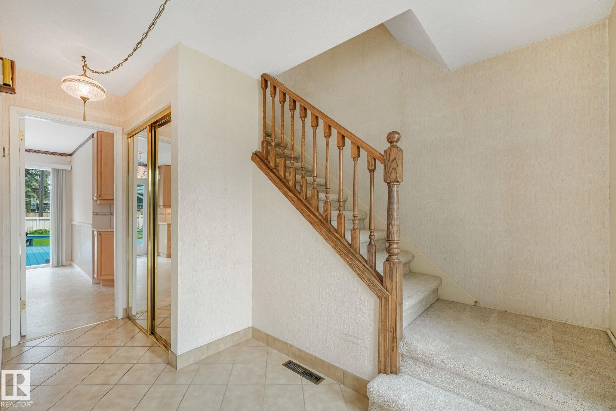 Entryway featuring a wood staircase with carpeted treads, a tiled floor, and a mirrored closet with gold-finish trim - 13320 79 Avenue Nw, Edmonton, AB - Indoor Photo Showing Other Room