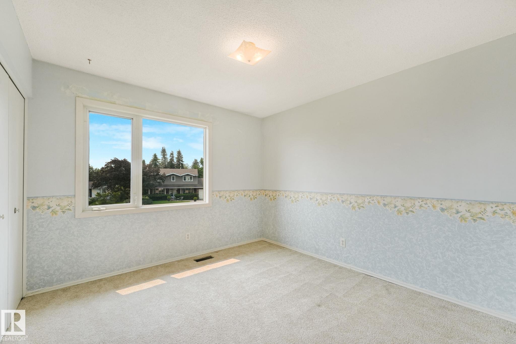 Bright room featuring a large window, light-colored carpet flooring, a ceiling-mounted light fixture, white trim, and a patterned wallpaper border - 13320 79 Avenue Nw, Edmonton, AB - Indoor Photo Showing Other Room