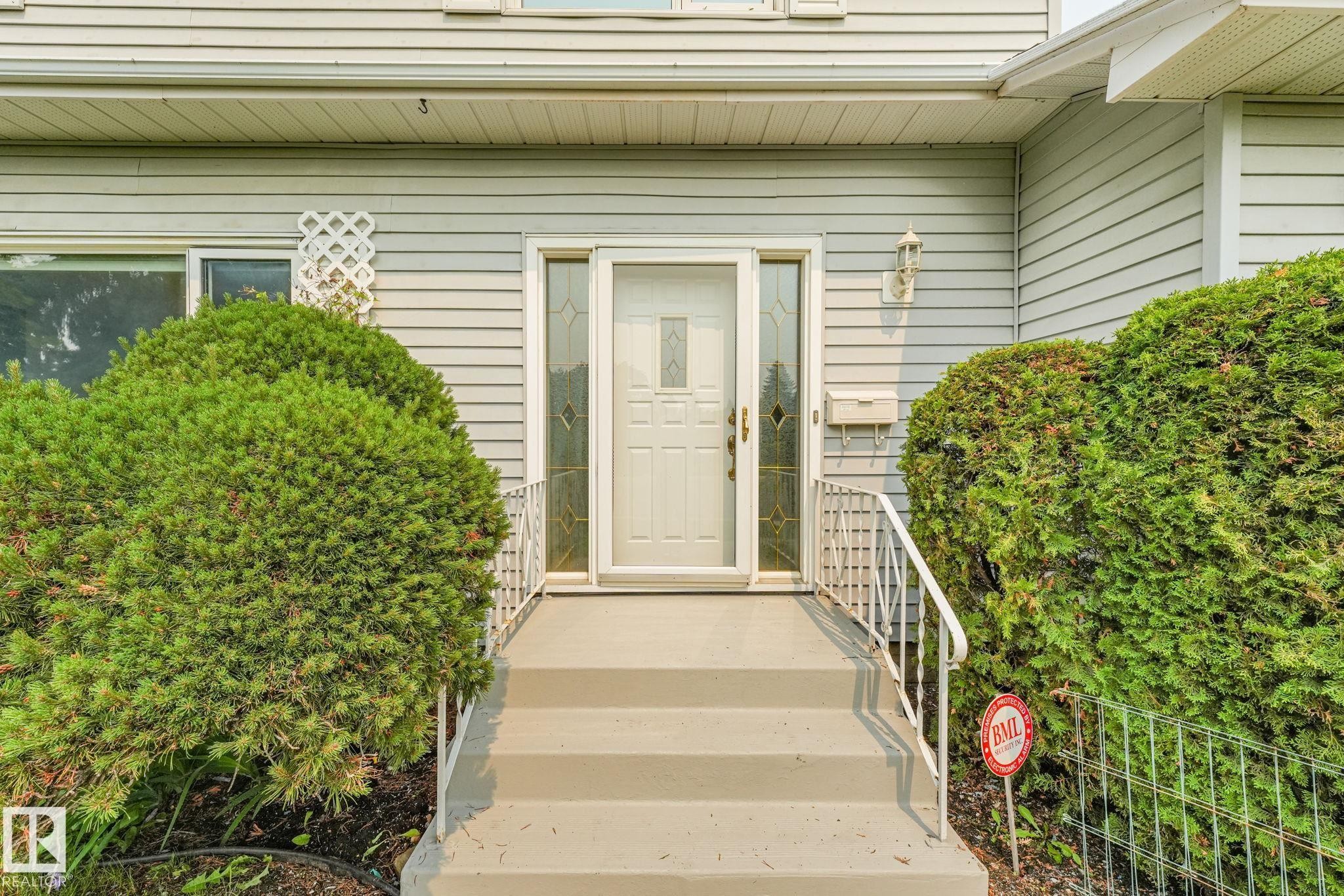 Entryway featuring a paneled door with decorative glass sidelights, light gray siding, concrete steps, and a white metal handrail - 13320 79 Avenue Nw, Edmonton, AB - Outdoor