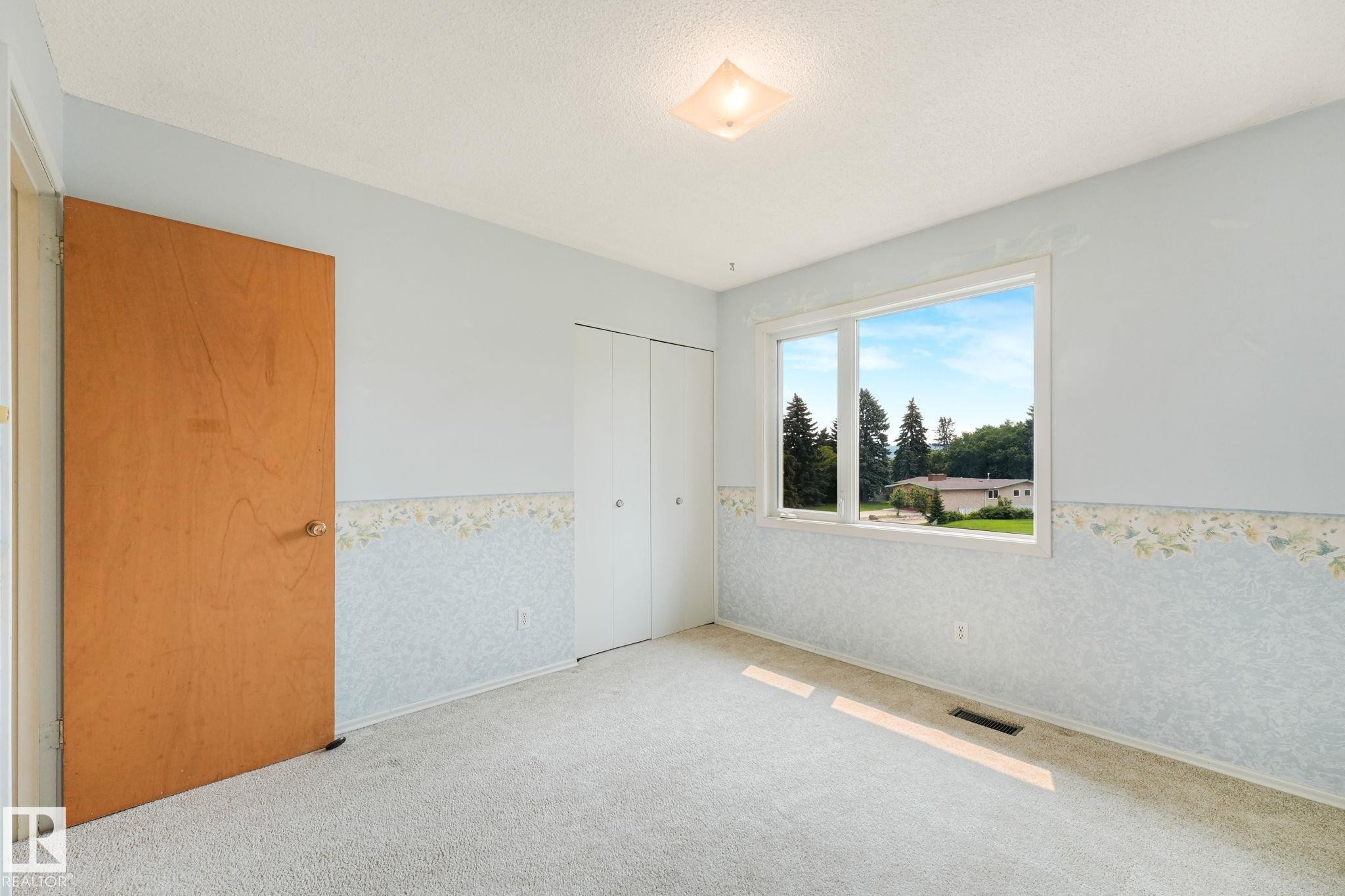 Carpeted room featuring a large window, a bi-fold closet, and a light wood door - 13320 79 Avenue Nw, Edmonton, AB - Indoor Photo Showing Other Room