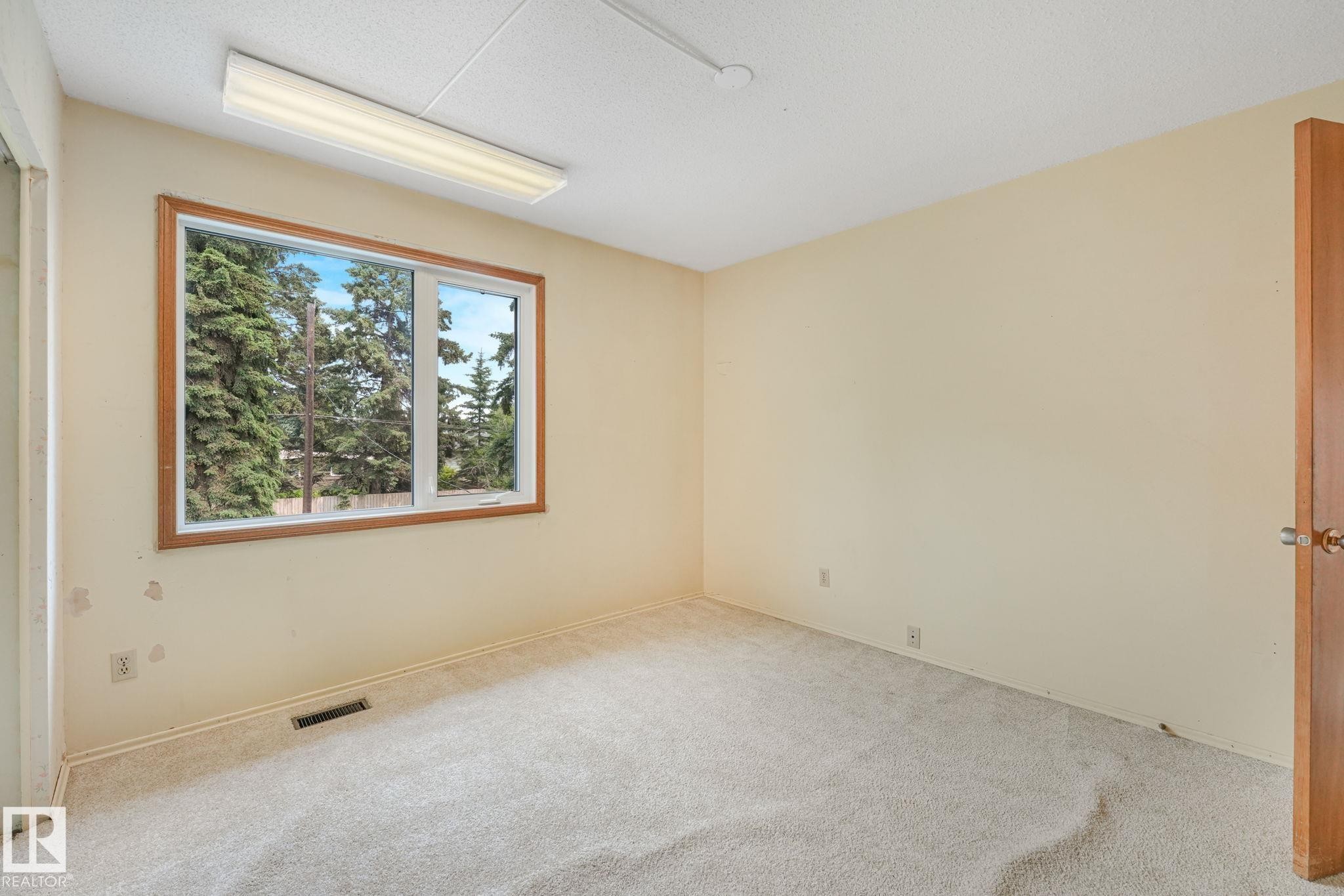 Carpeted room featuring a large window with a wood-finish frame, a horizontal fluorescent light fixture, and a wood-panel door - 13320 79 Avenue Nw, Edmonton, AB - Indoor Photo Showing Other Room