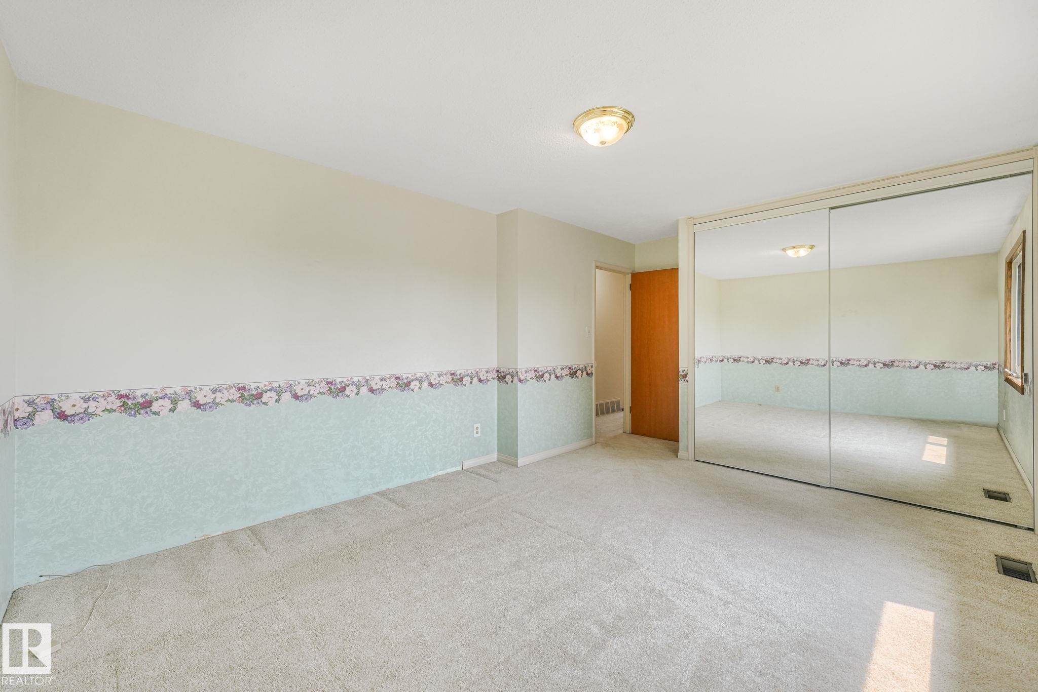 Carpeted room featuring a ceiling-mounted light fixture, full-height mirrored closet doors, and wood-trim windows - 13320 79 Avenue Nw, Edmonton, AB - Indoor Photo Showing Other Room