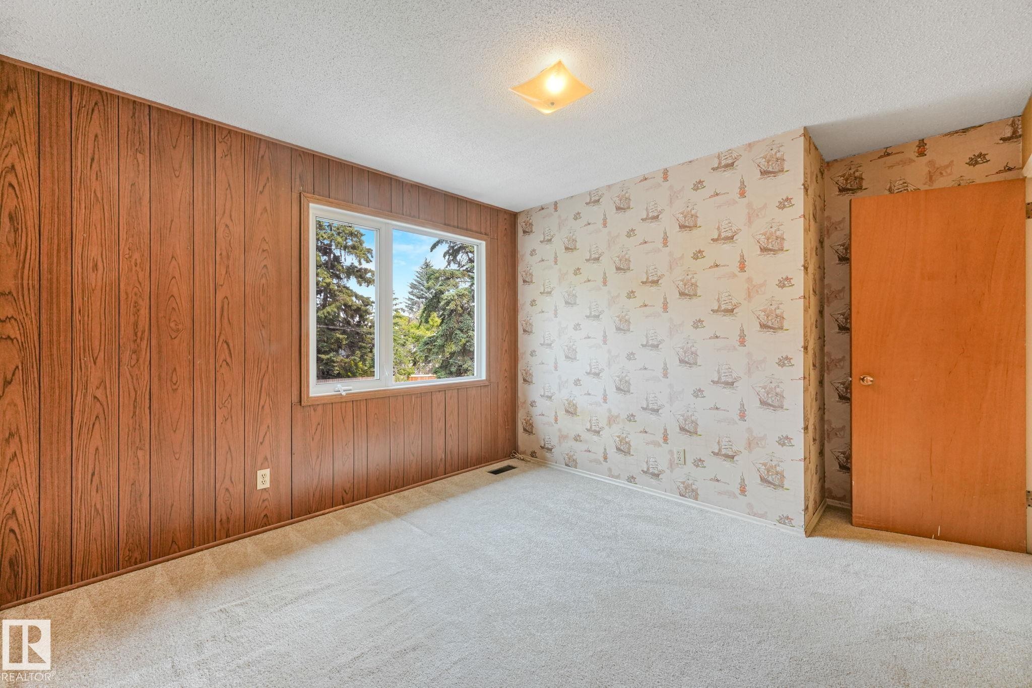 Room featuring wood paneling, a large window, patterned wallpaper, a wood-finish door, and neutral carpeting - 13320 79 Avenue Nw, Edmonton, AB - Indoor Photo Showing Other Room