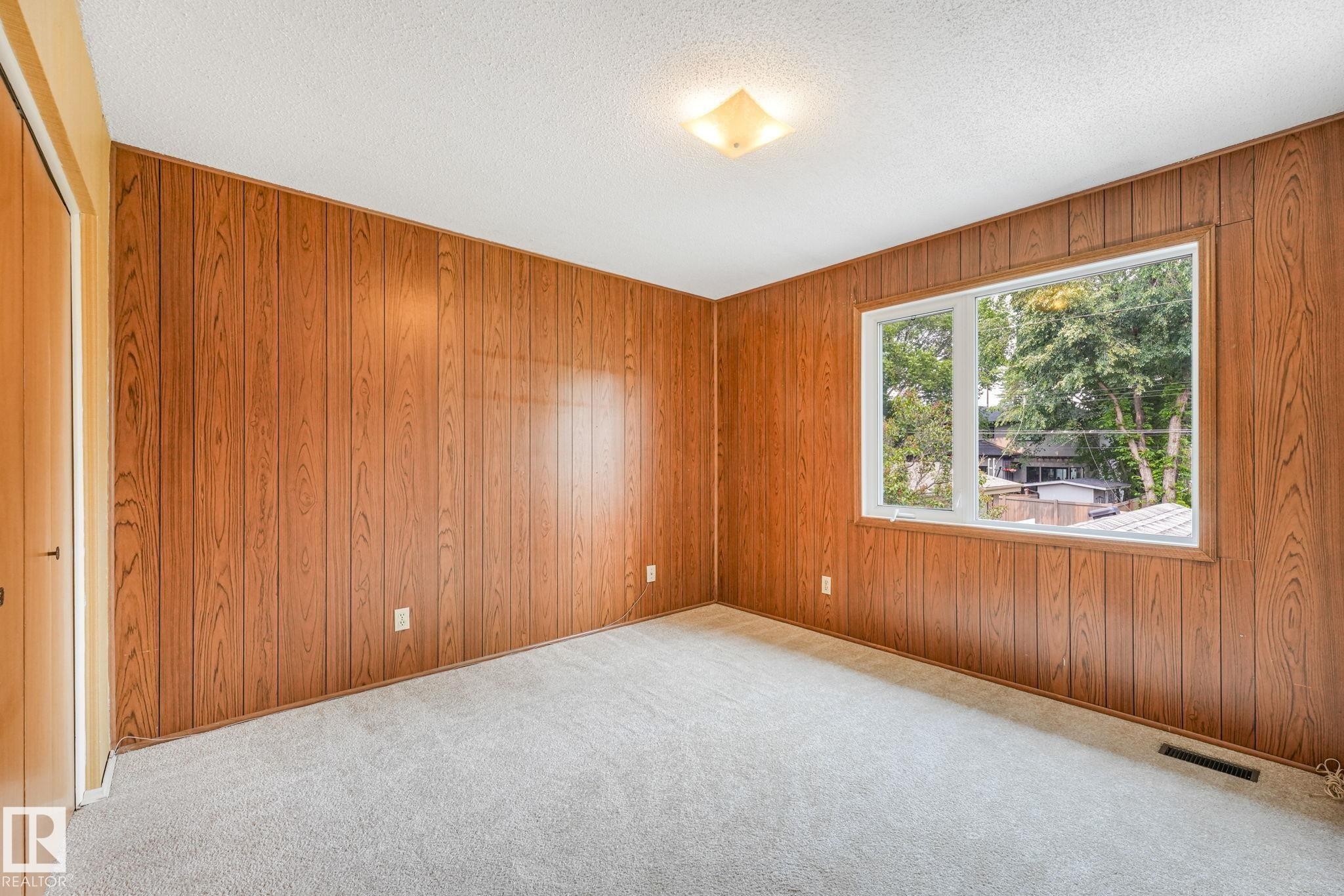 Room featuring wood-paneled walls, a large window, light-toned carpet flooring, a closet with a wood-finish door, and a ceiling-mounted light fixture - 13320 79 Avenue Nw, Edmonton, AB - Indoor Photo Showing Other Room