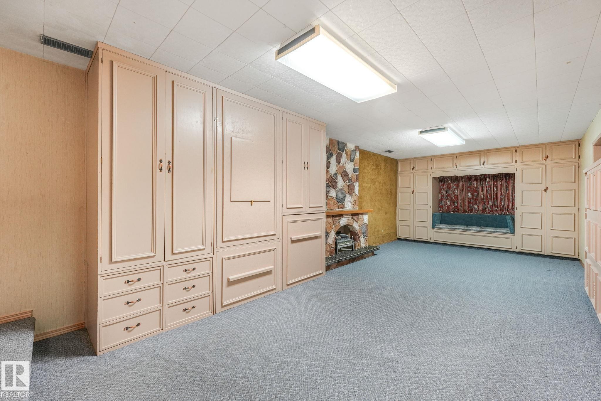 Spacious room featuring extensive built-in cabinetry, a stone-clad fireplace, and recessed window seating - 13320 79 Avenue Nw, Edmonton, AB - Indoor Photo Showing Other Room