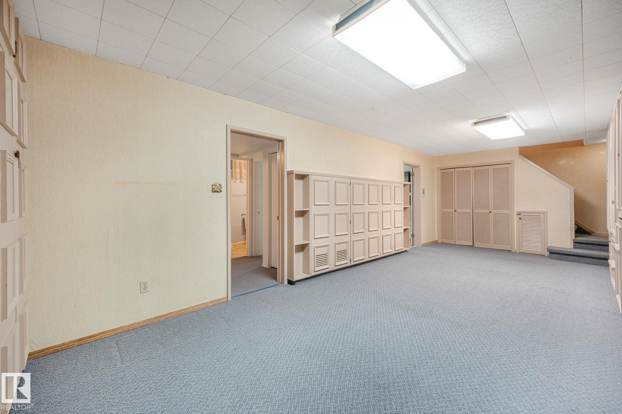 Spacious interior room featuring light blue carpeting, a drop ceiling with recessed lighting, and built-in white cabinetry - 13320 79 Avenue Nw, Edmonton, AB - Indoor